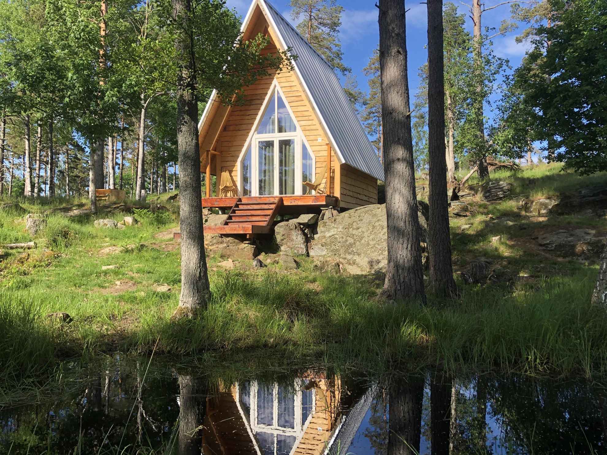 Een A-vormige hut met houten paneel is gelegen in de natuur aan een meer.