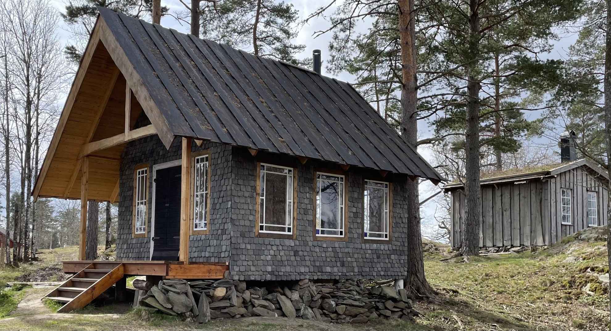 Een leistenen huis met houten lambrisering gelegen in de natuur.