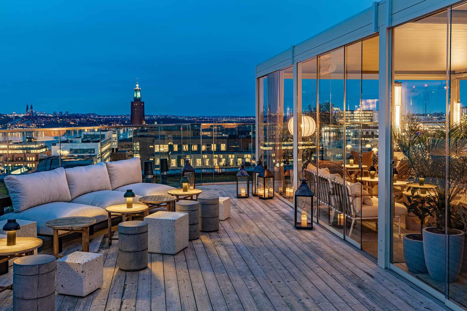 Een stijlvolle buitenbar op een dakterras met uitzicht over Stockholm en het stadhuis. Rechts zie je een gedeelte dat achter een glazen wand zit.
