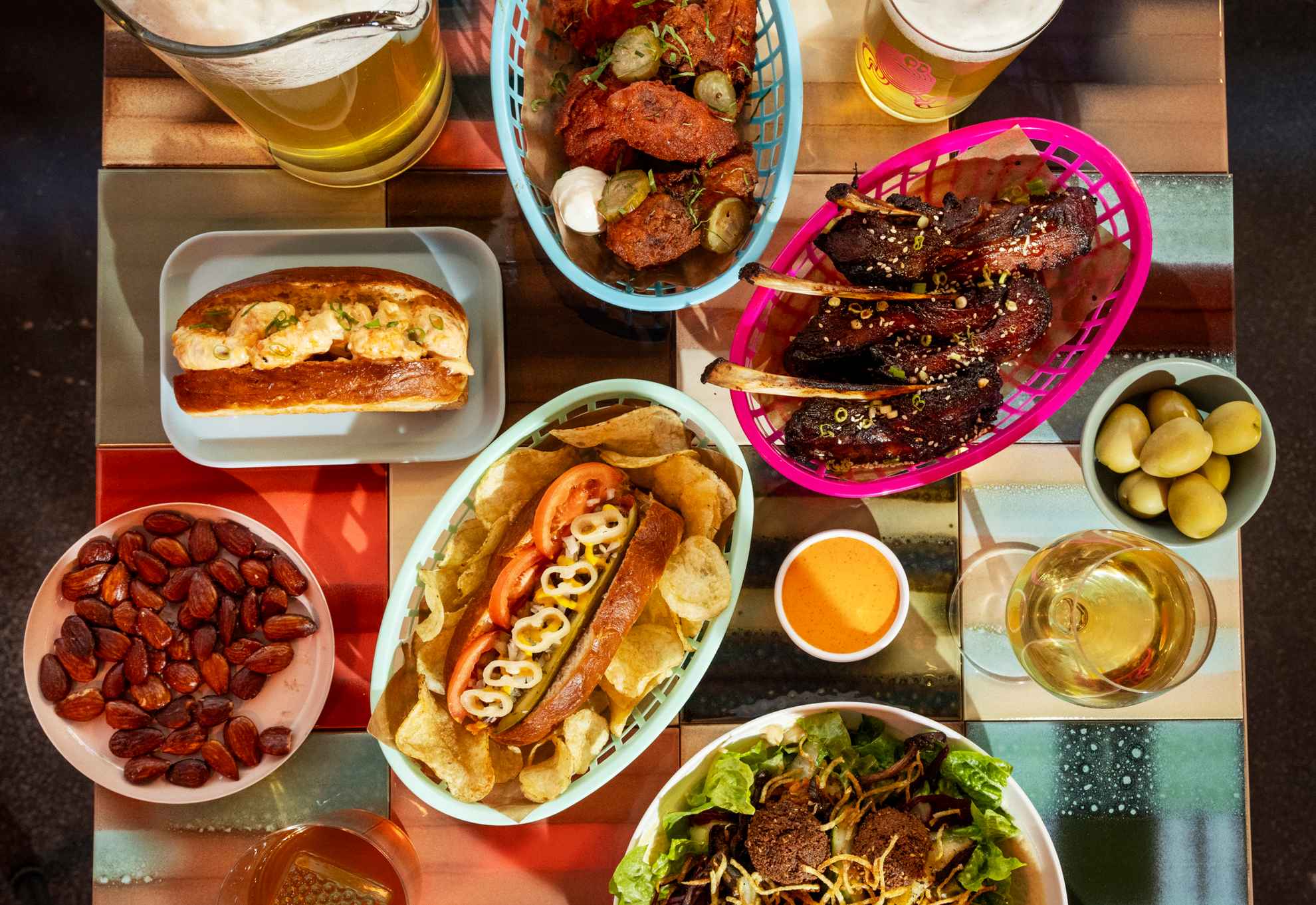 Een vierkante tafel gevuld met kleurrijk streetfood in verschillende manden en op borden, maar ook glazen bier en wijn.