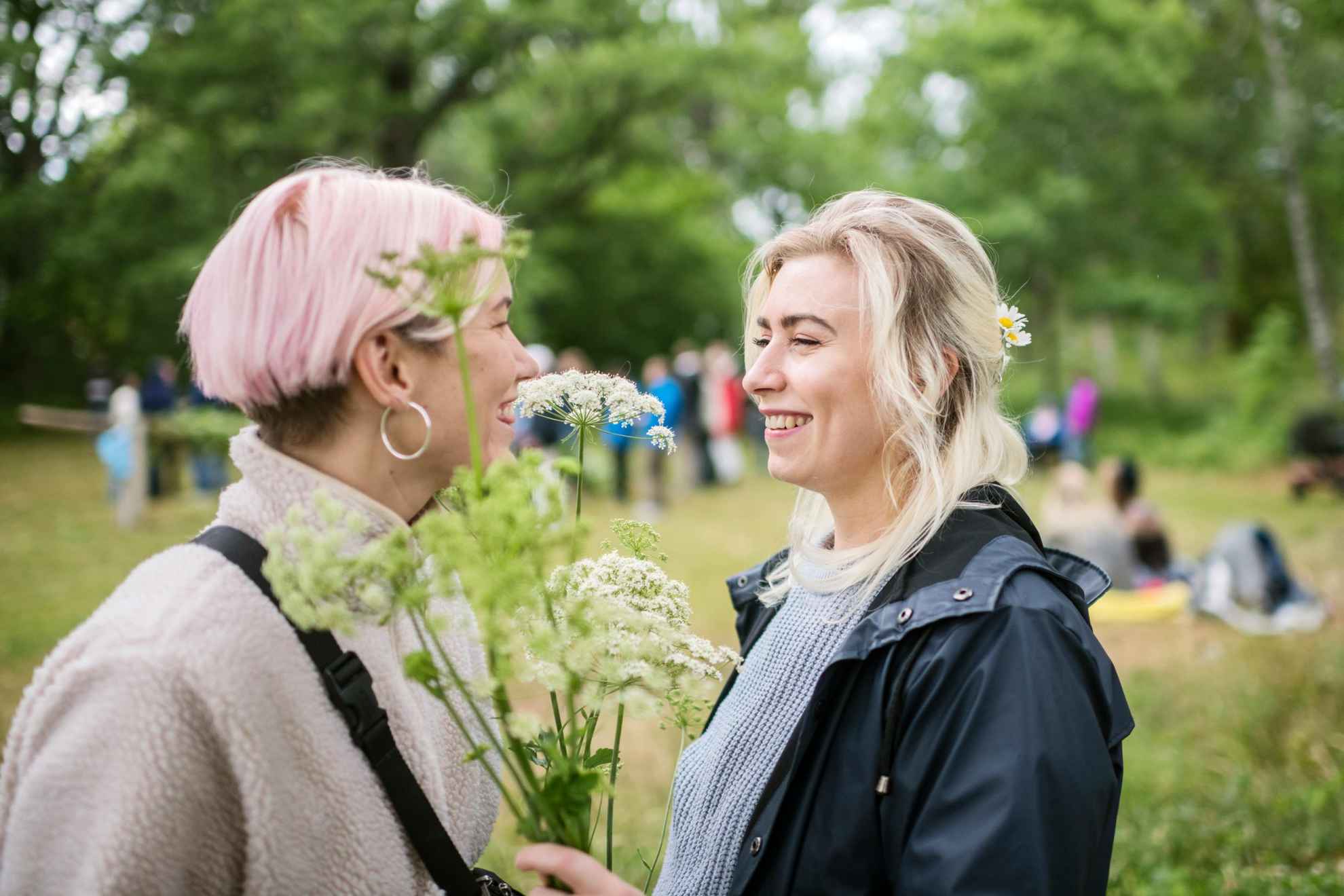 Twee vrouwen met bloemen in hun handen glimlachen naar elkaar.
