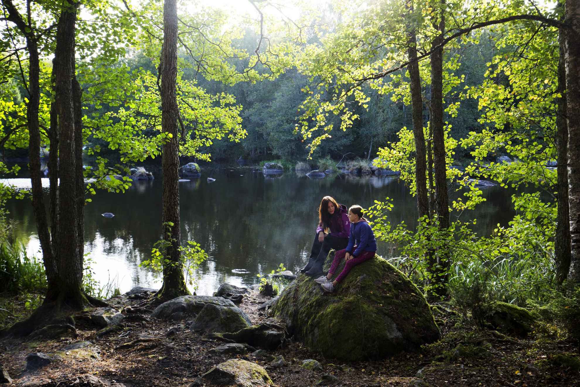 Twee meisjes zitten op een rots naast een meer in de natuur.