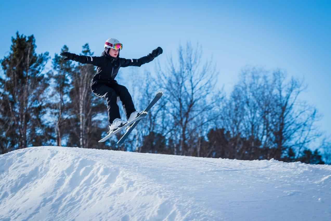 Een kind dat op ski's bovenop een skihelling springt.