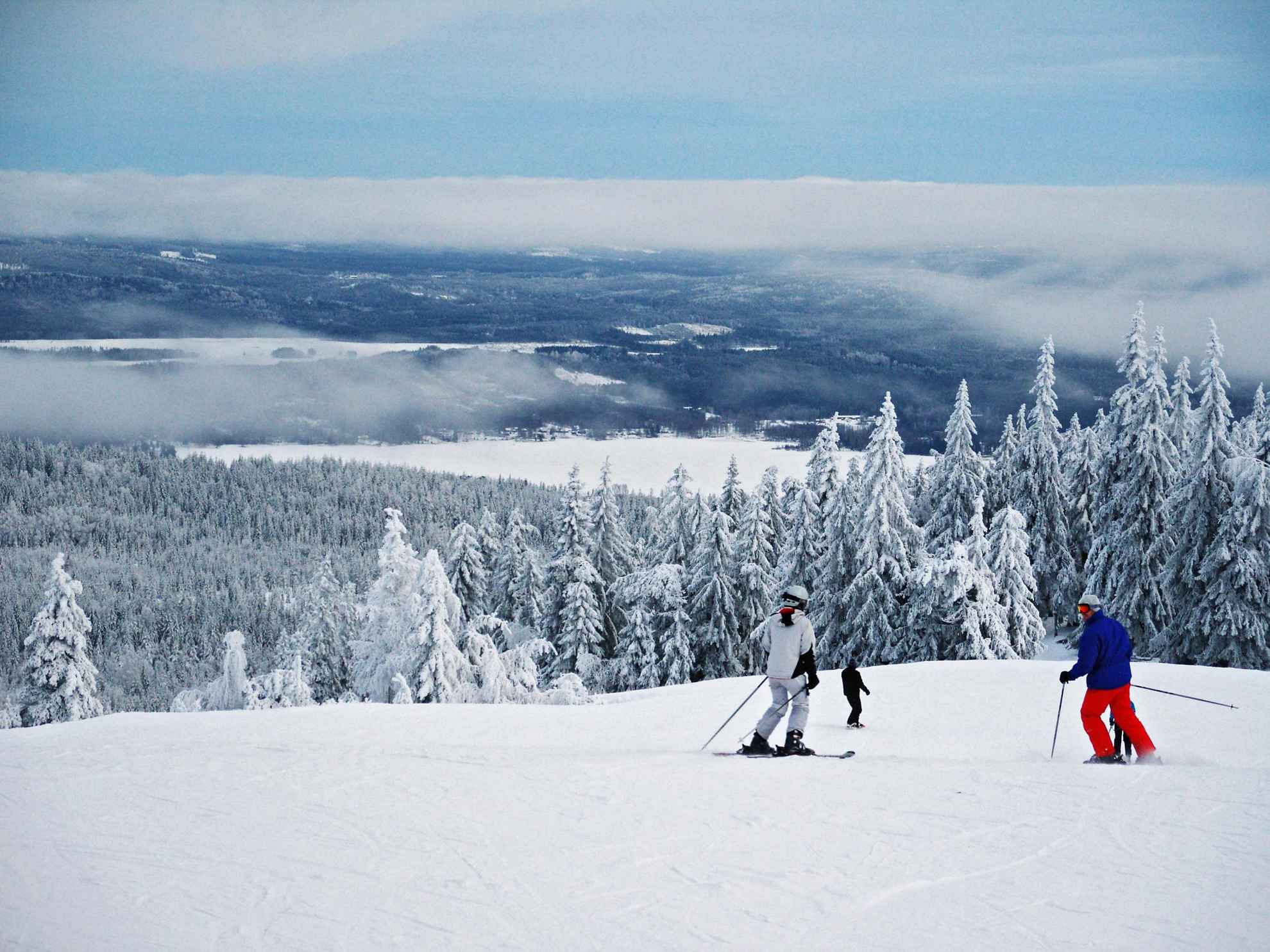 Een uitzicht vanaf een besneeuwde berg. Mensen skiën de skipiste af.