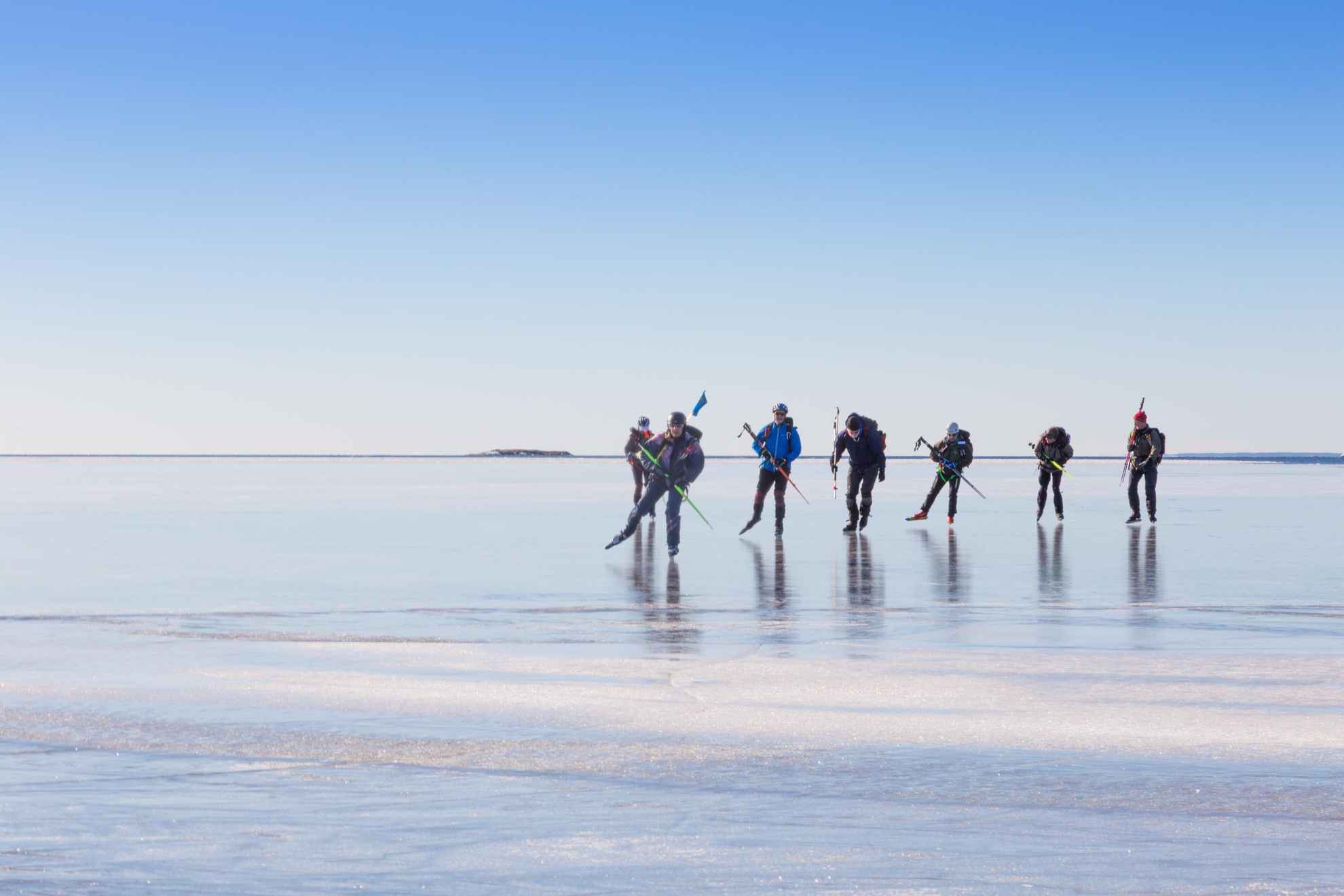 Zeven mensen schaatsen lange afstand op helder ijs op een zonnige winterdag.