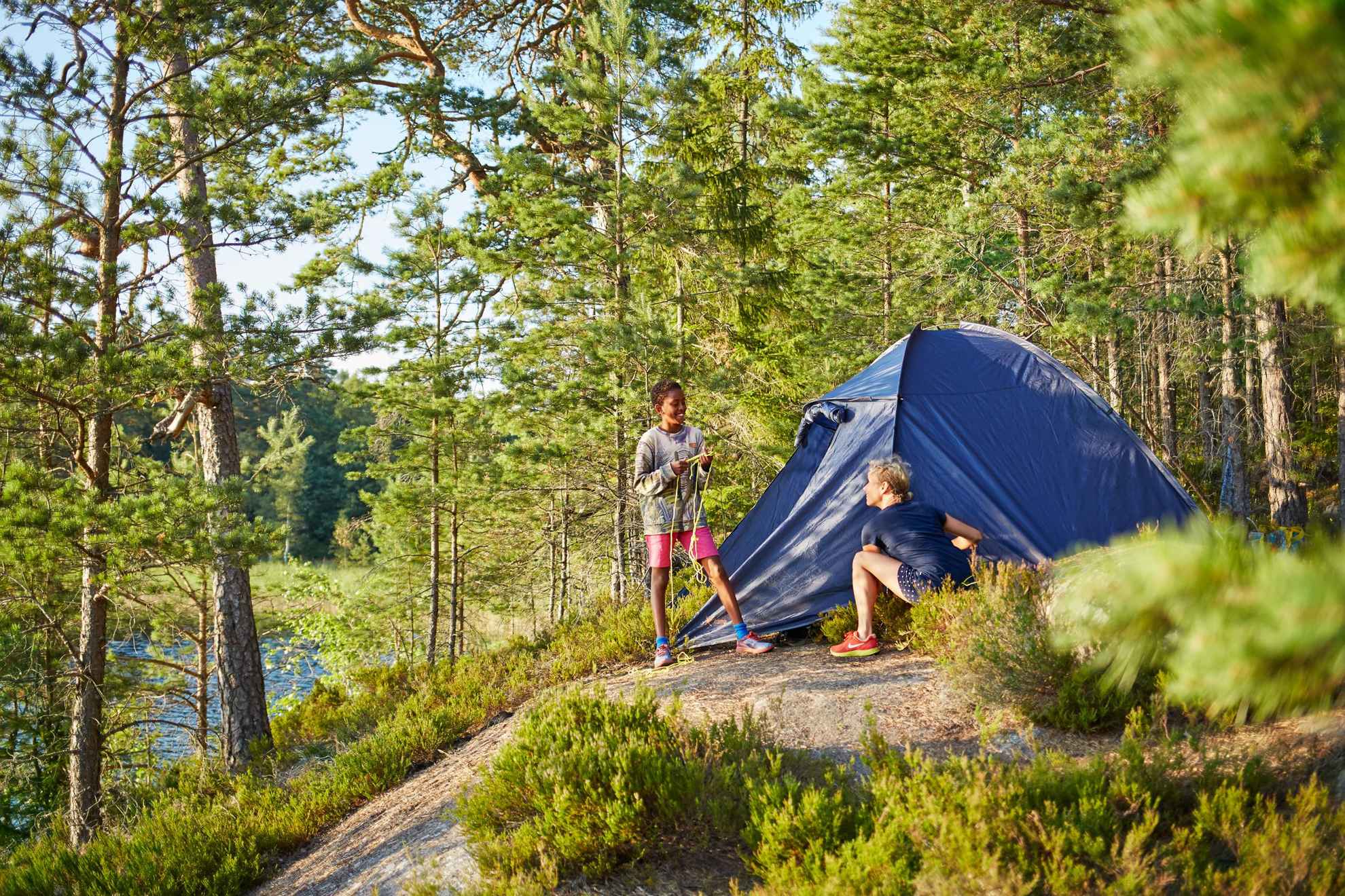 Twee mensen in Zweden zitten bij een tent in het bos naast een meer.