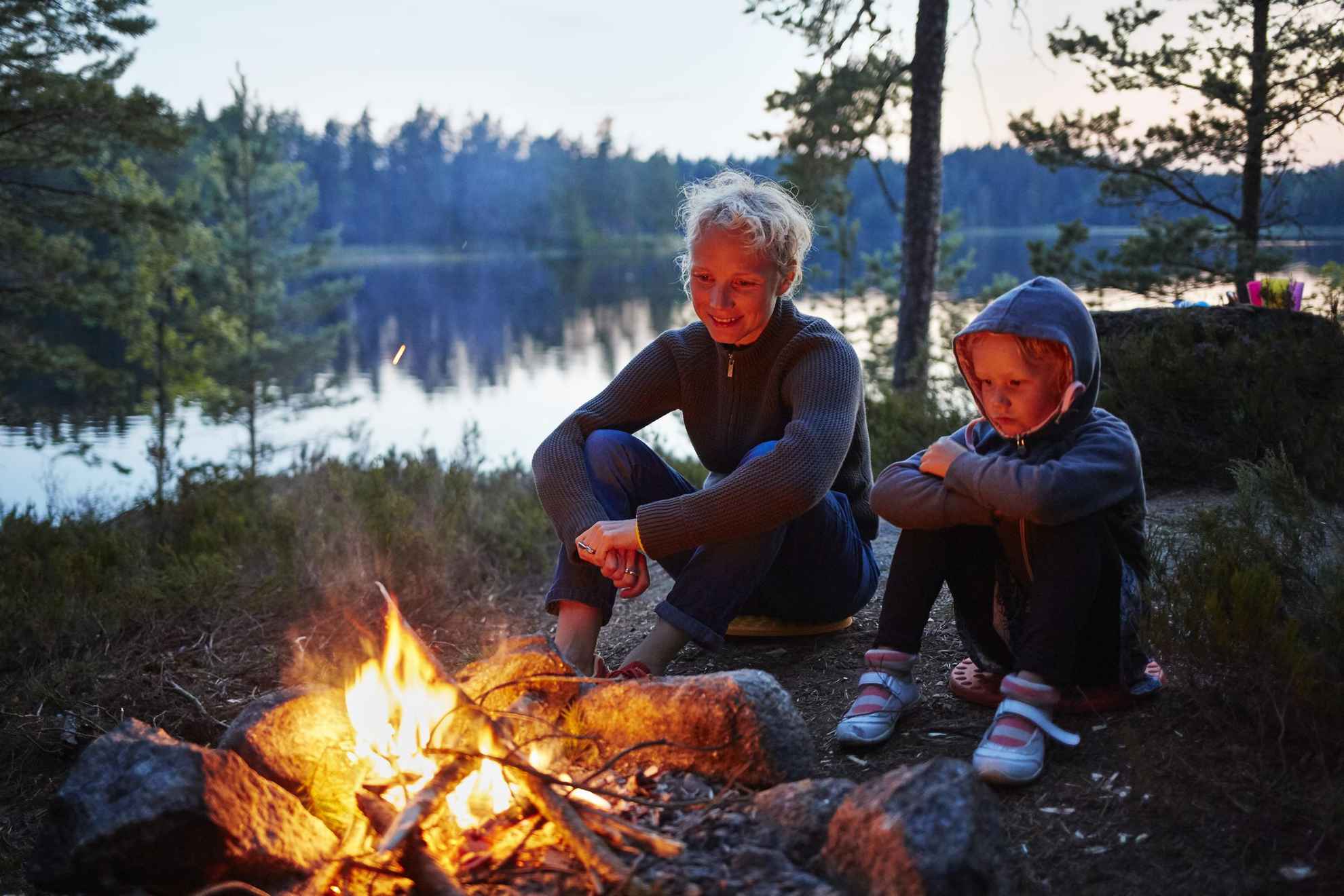 Het is avond en twee mensen in Zweden zitten bij een vuur in het bos naast een meer.
