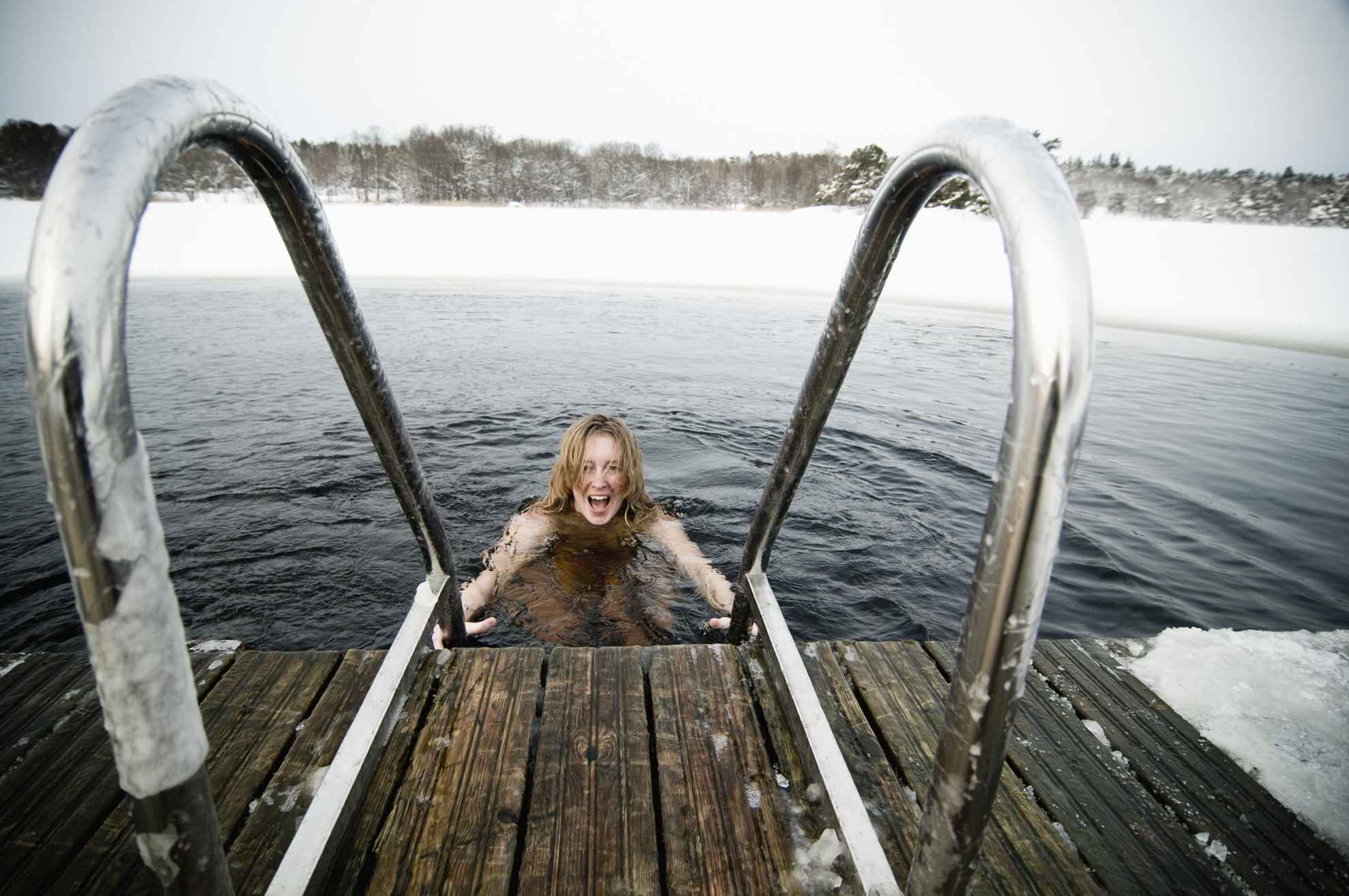 Een vrouw hapt naar adem terwijl ze afdaalt in een ijsbad. IJzige bomen op de achtergrond.
