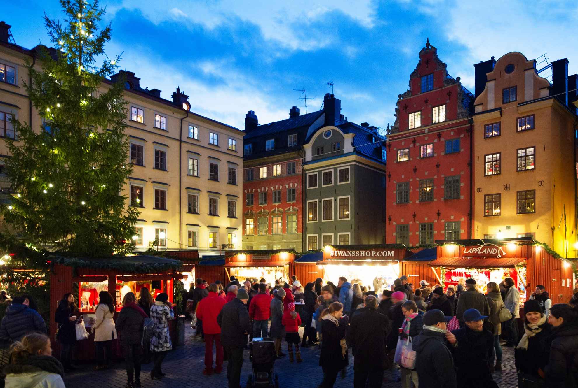 Massa's mensen bezoeken de kraampjes van de ouderwetse kerstmarkt in de oude binnenstad van Stockholm, naast een verlichte kerstboom.