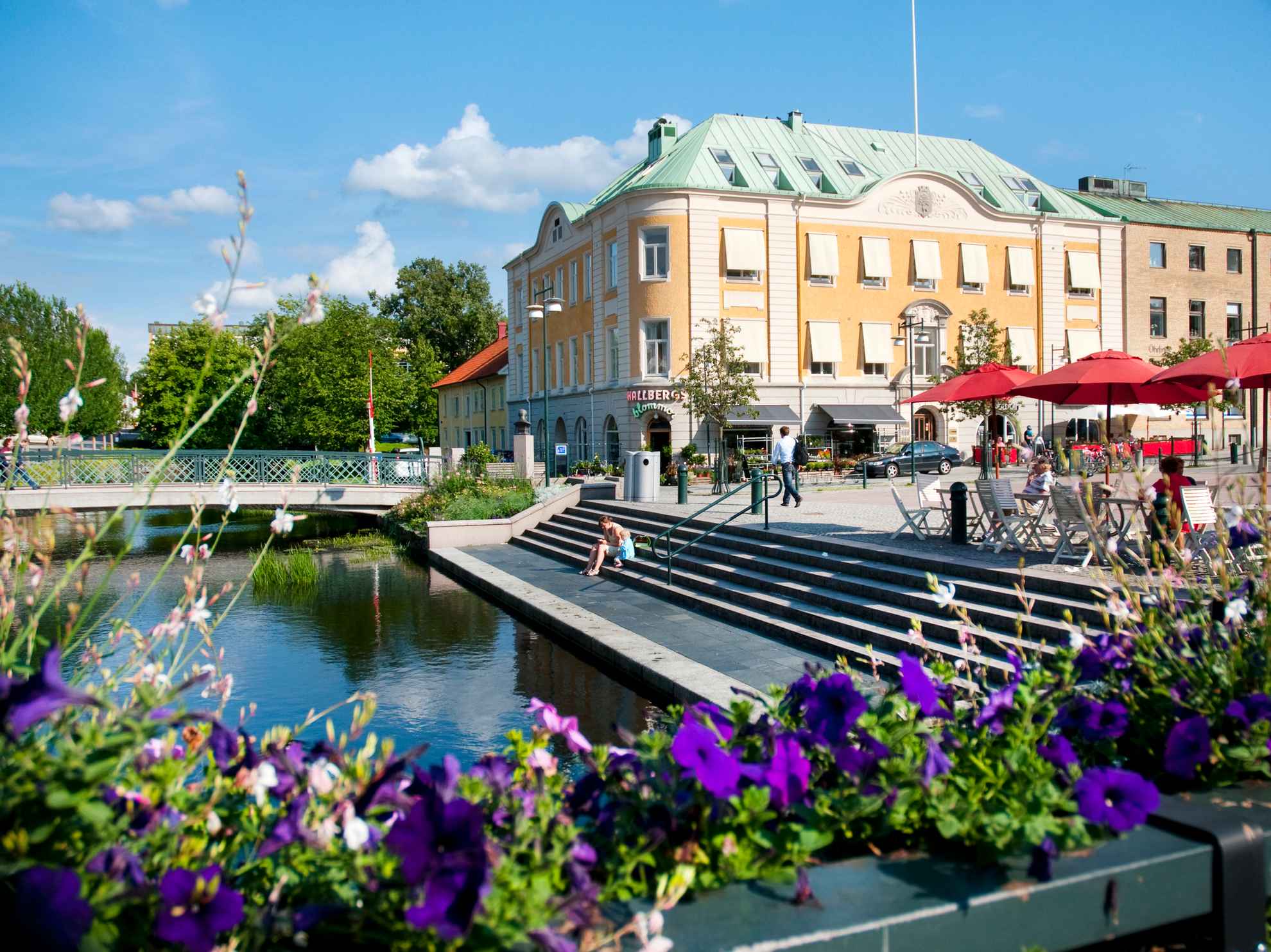 Zonnige dag in Alingsås. Stadscentrum met trappen en een brug over Lillån. Paarse bloemen op de voorgrond.