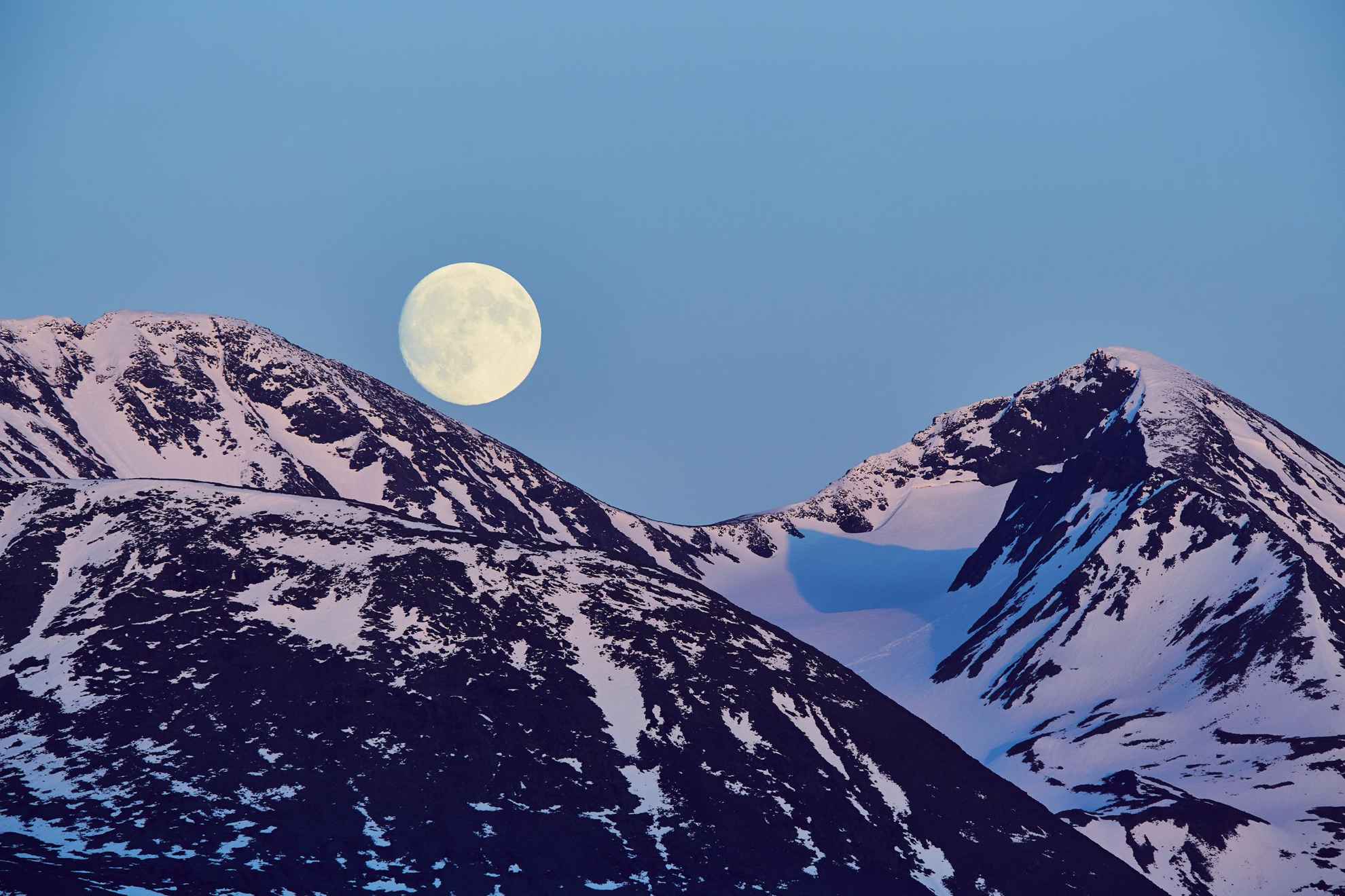 Twee besneewde bergtoppen en de maan.