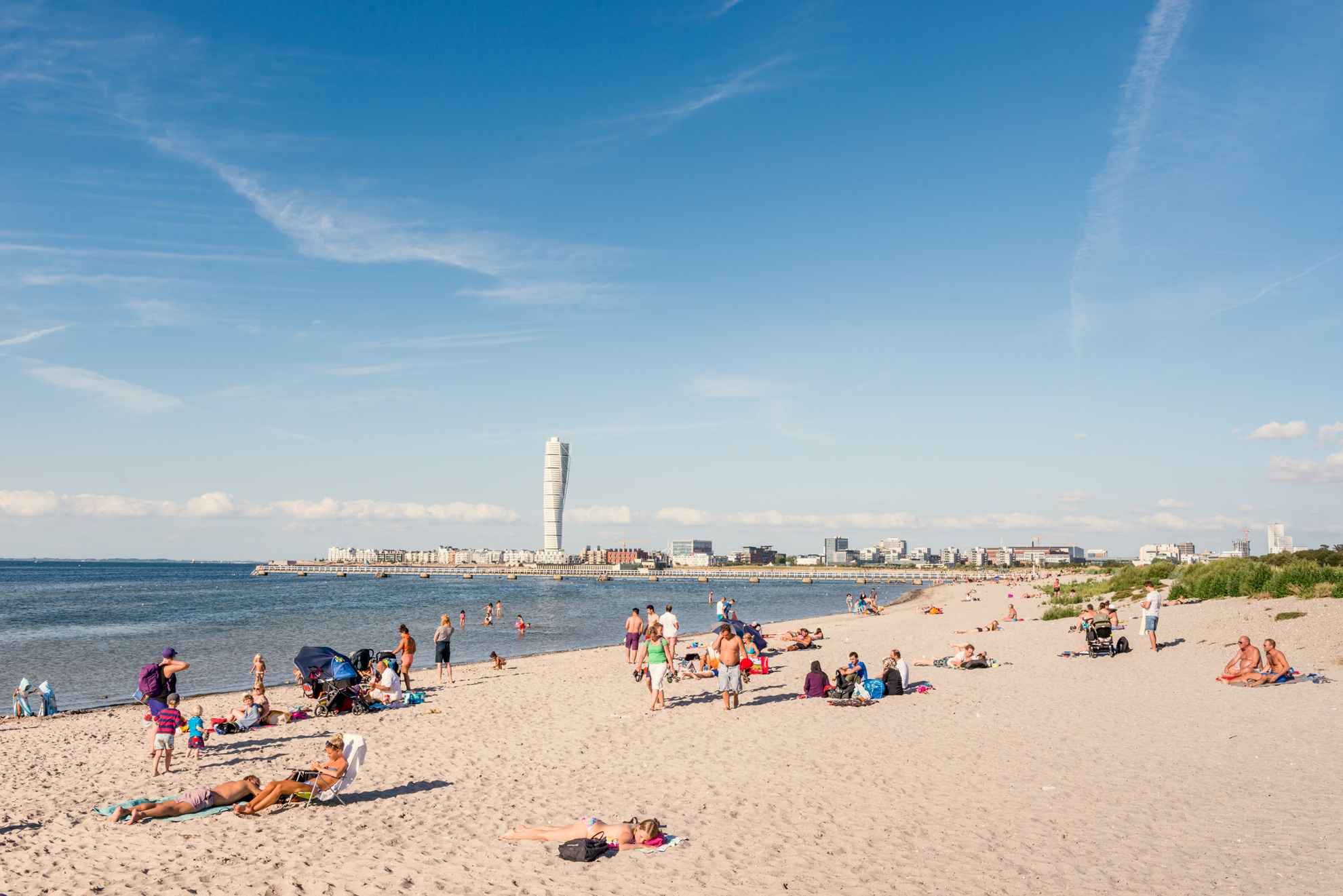 Mensen genieten op een strand in Malmö. Aan de horizon kun je het gebouw "Turning Torso" zien.