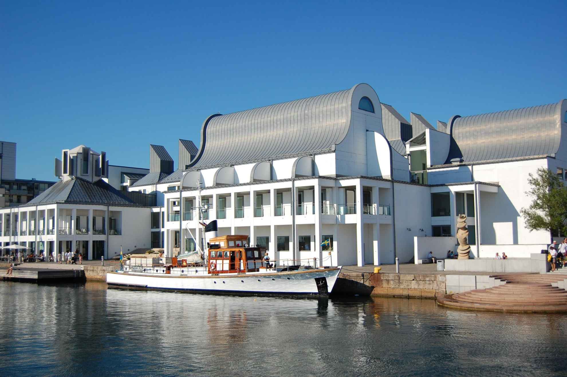 Een groot wit huis, met een grijs gebogen dak, gelegen aan de haven in de haven.