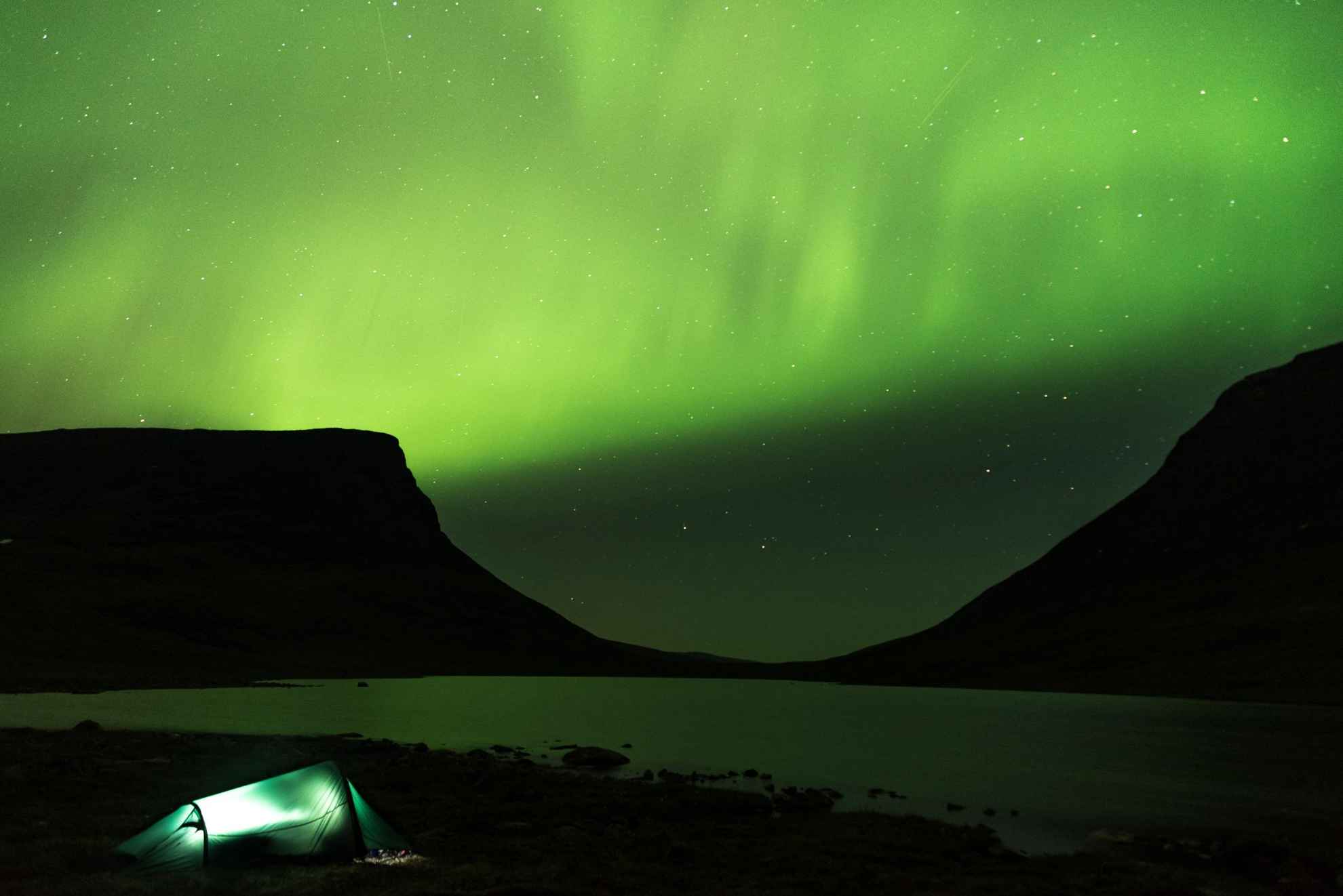 Noorderlicht danst boven de Lapporten-bergen in Abisko. Bij het Torne-meer wordt een opgezet tent van binnenuit verlicht.