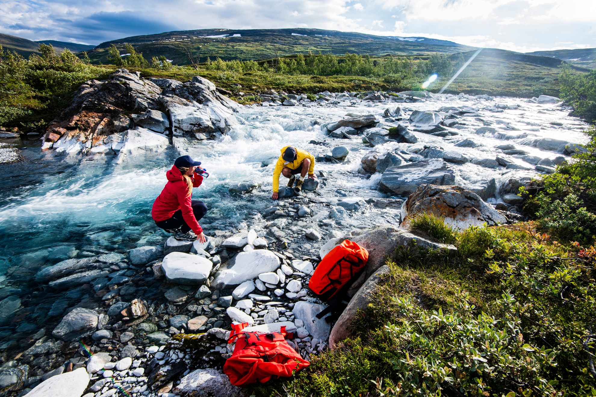 Twee mensen drinken uit een rivier in Zweeds Lapland.