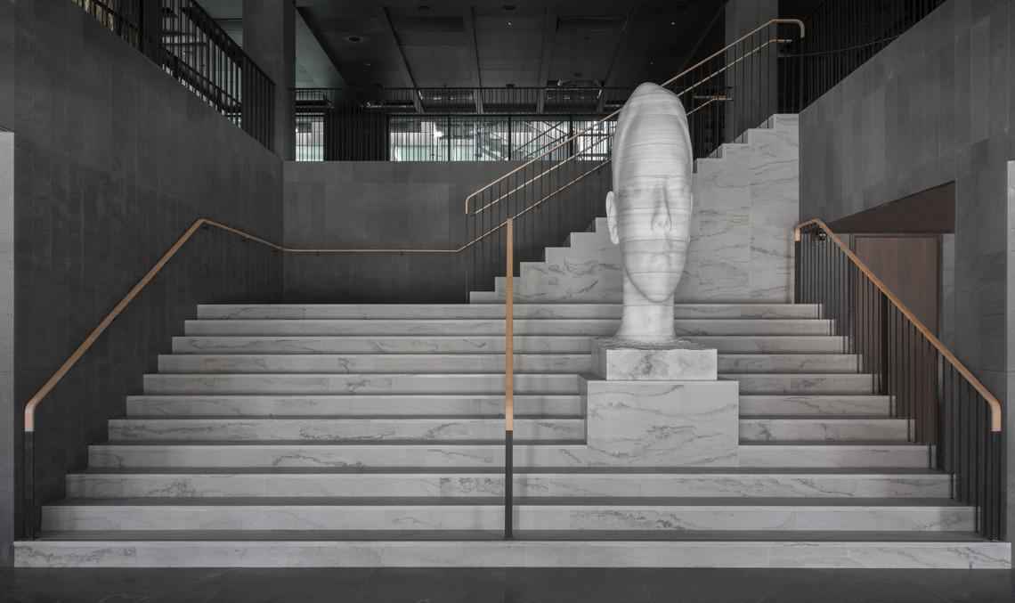 Op een marmeren trap staat een marmeren sculptuur van een hoofd.