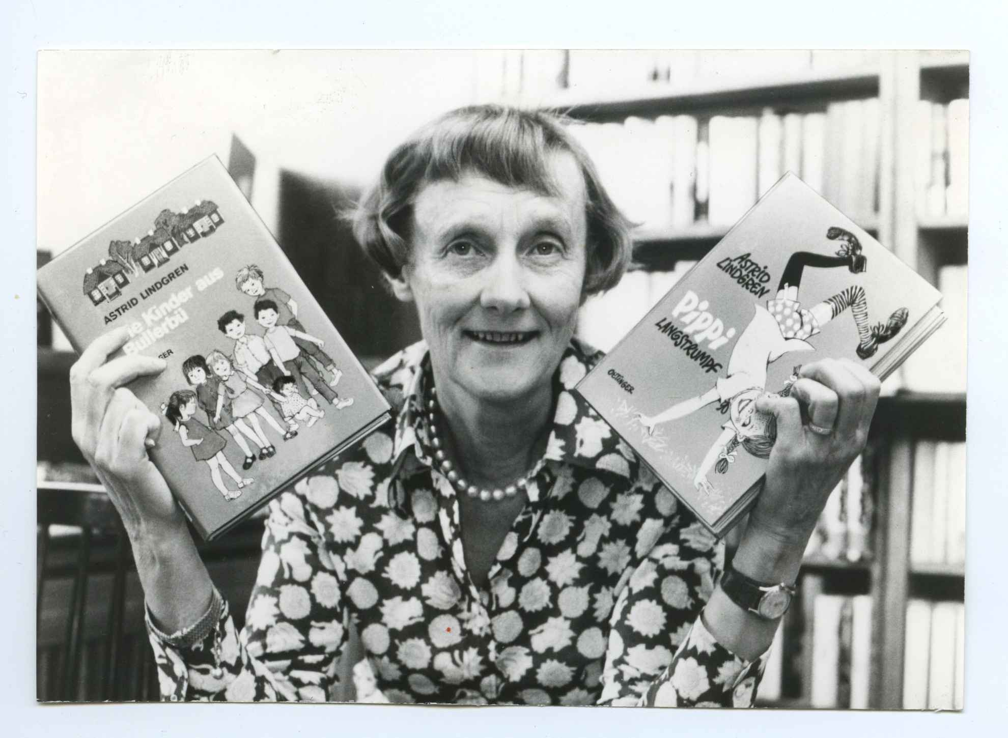 Een zwart-wit portret van de schrijfster Astrid Lindgren met haar boek Pippi Langkous in de ene hand en het boek De Noisy Village-kinderen in de andere hand.
