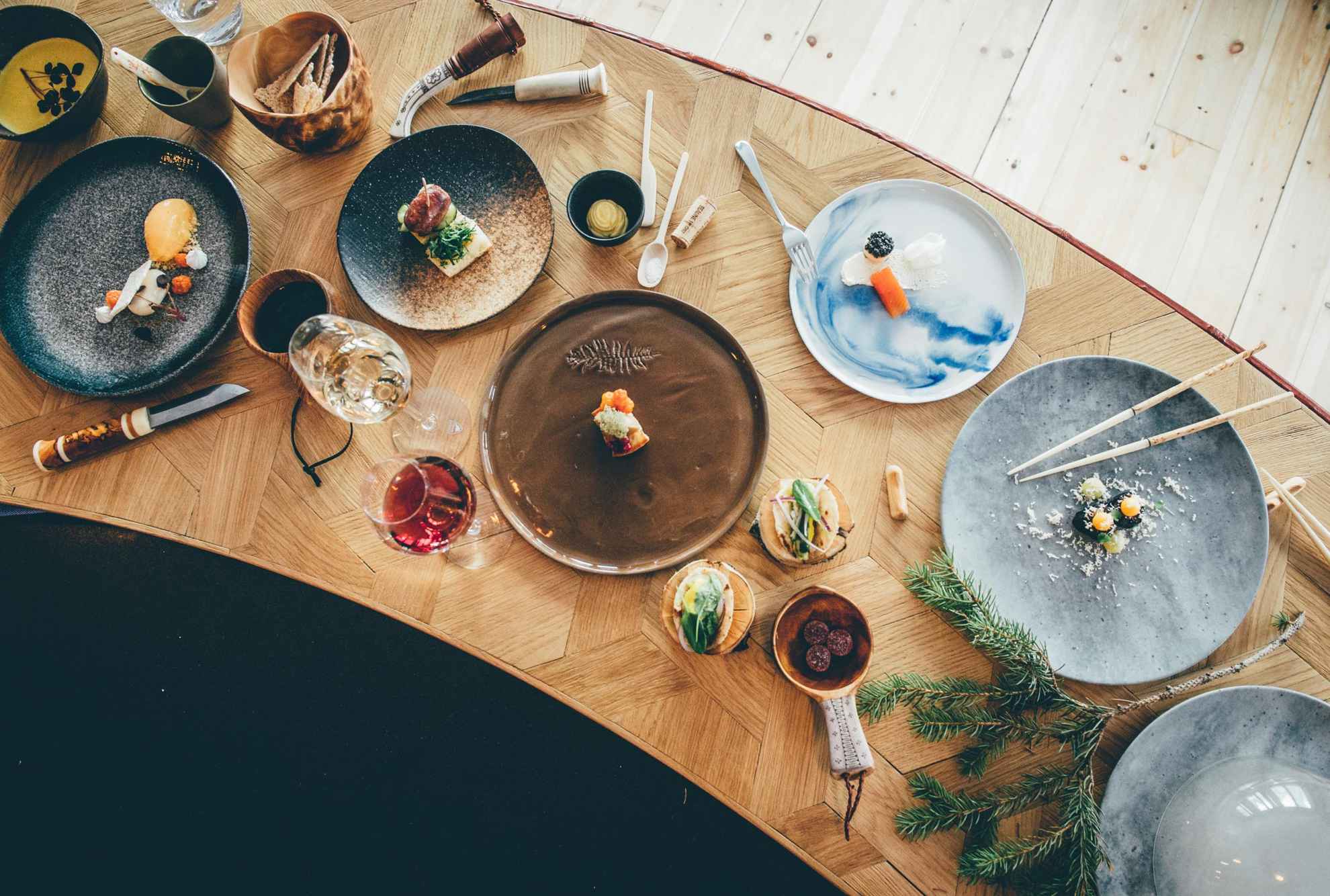 Een houten tafel met eten, borden, wijnglazen en bestek.