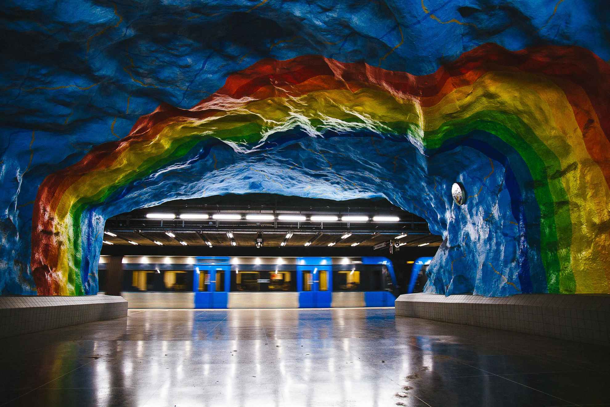 Rotsen in regenboogkleuren. Op de achtergrond een blauwe metro.