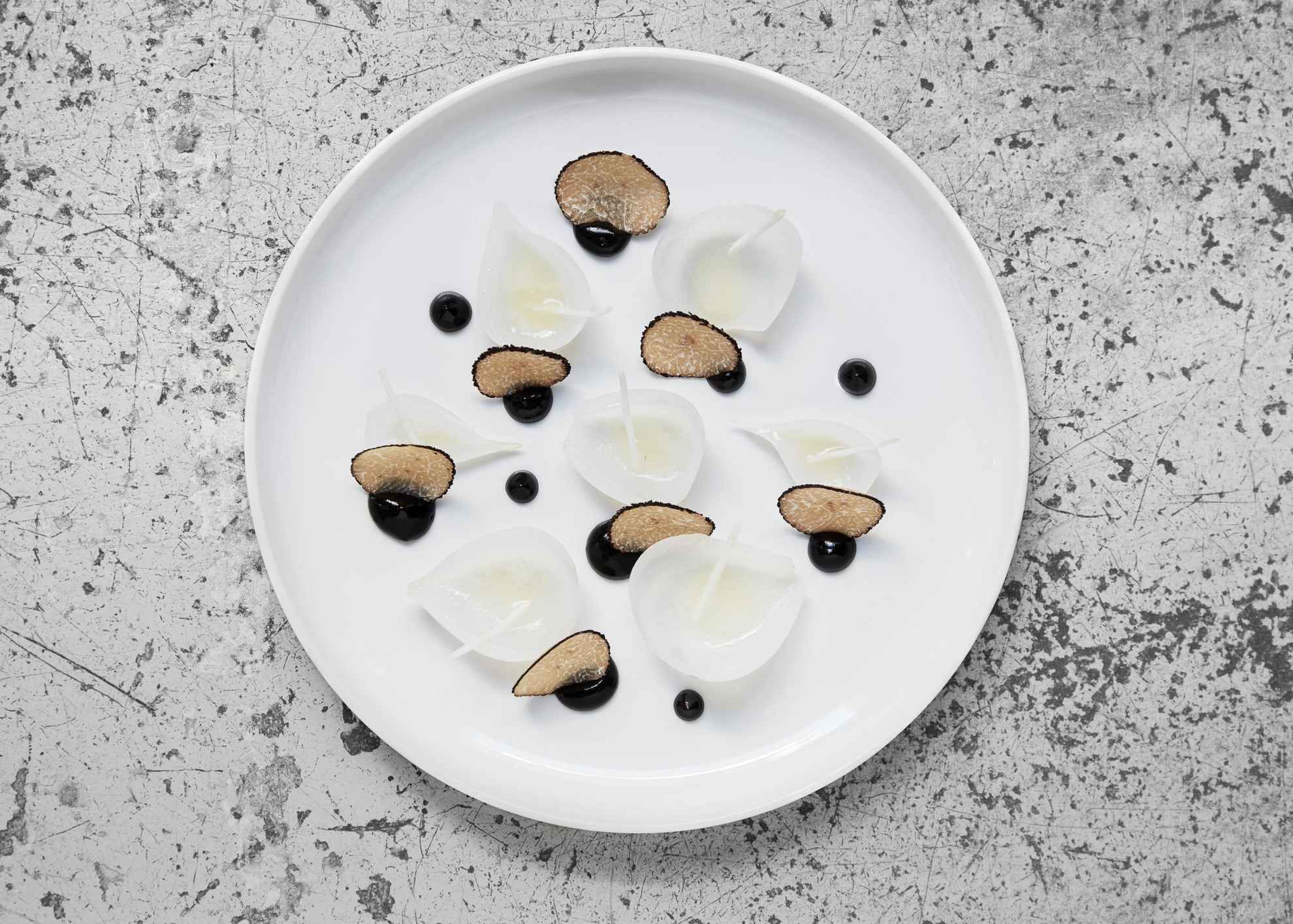 Close-up on a stylish dish with lightly pickled silver onion with black truffle & a vinaigrette on a white plate.