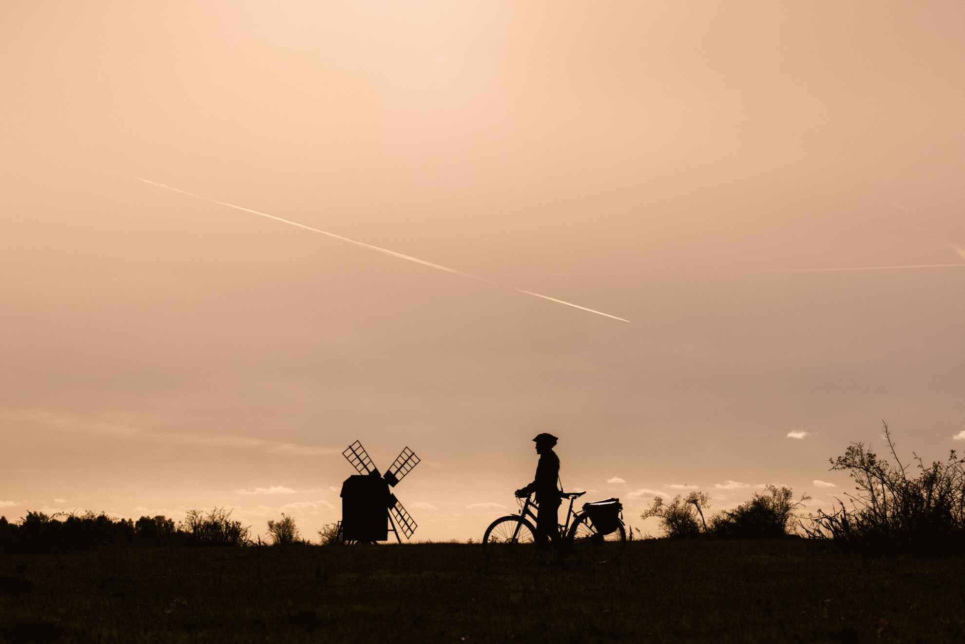 Silhouet van een fietser in de schemering met een windmolen op de achtergrond.