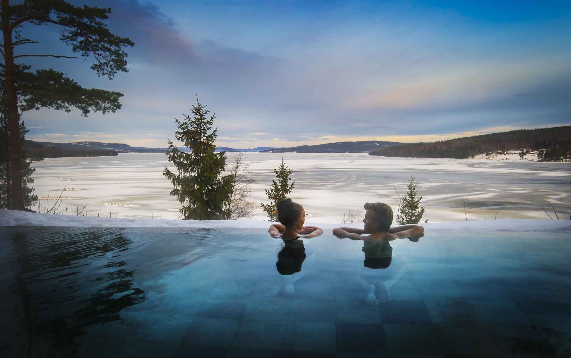 Twee mensen ontspannen in het buitenzwembad van Orbaden Spa & Resort in Hälsingland, kijkend naar het besneeuwde water.