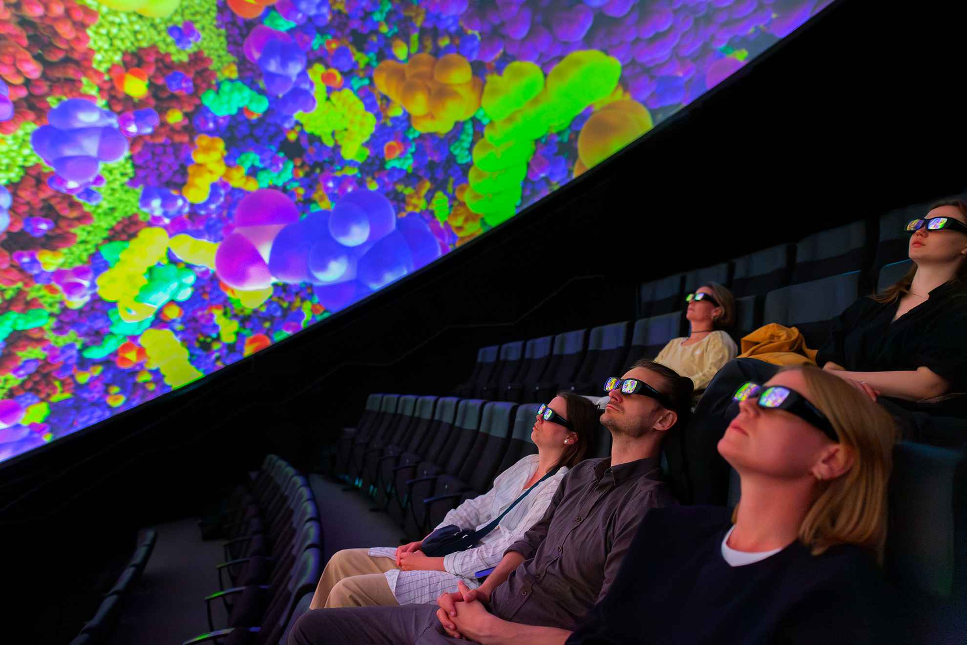 Een groep mensen met een 3D-bril zit in stoelen en kijkt naar het scherm in de Wisdome Stockholm.