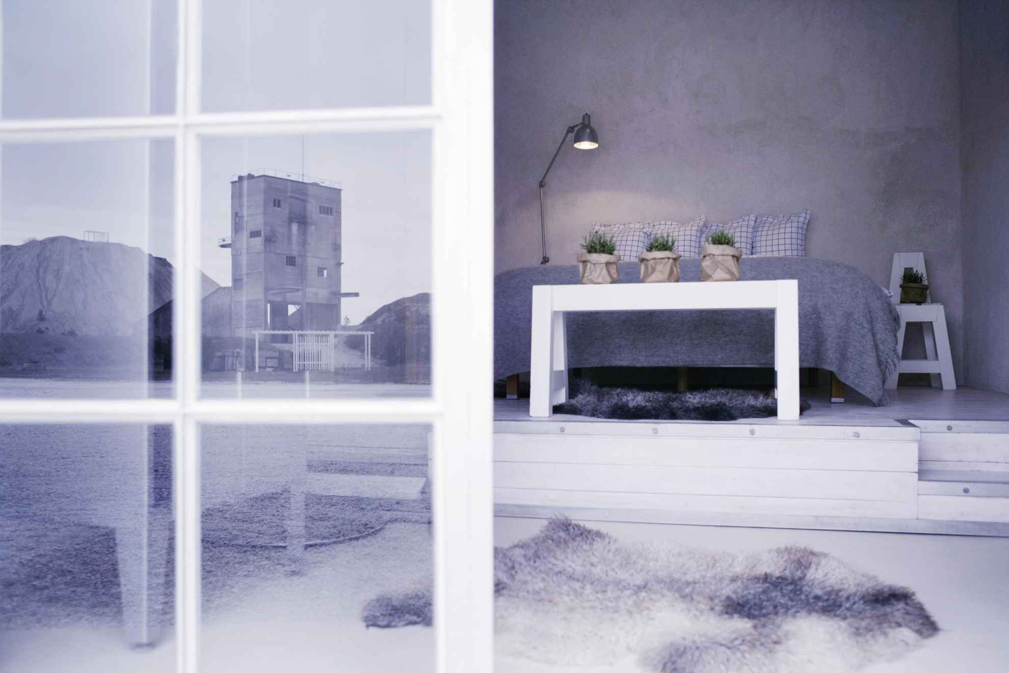 Minimalistisch ontworpen hotelkamer met een kalksteenfabriek die wordt weerspiegeld in een raam in Furillen Fabriken, Gotland.