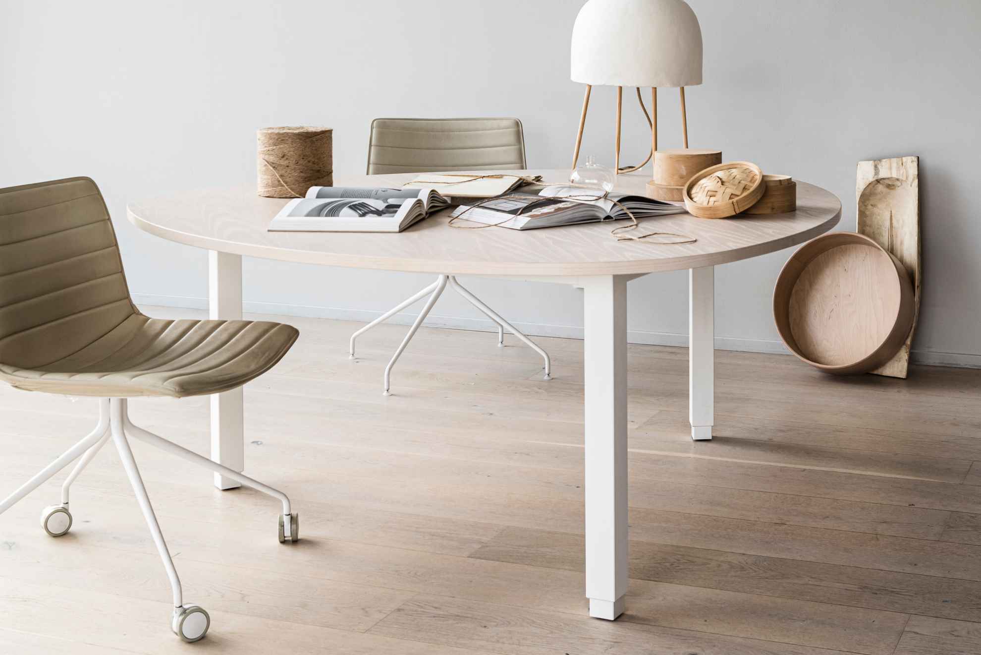 Een design tafel van lichtgekleurd hout op een lichtgekleurde houten vloer. Ernaast staat een bureaustoel op wielen. Op de tafel staan twee opengeslagen boeken en twee houten potten.