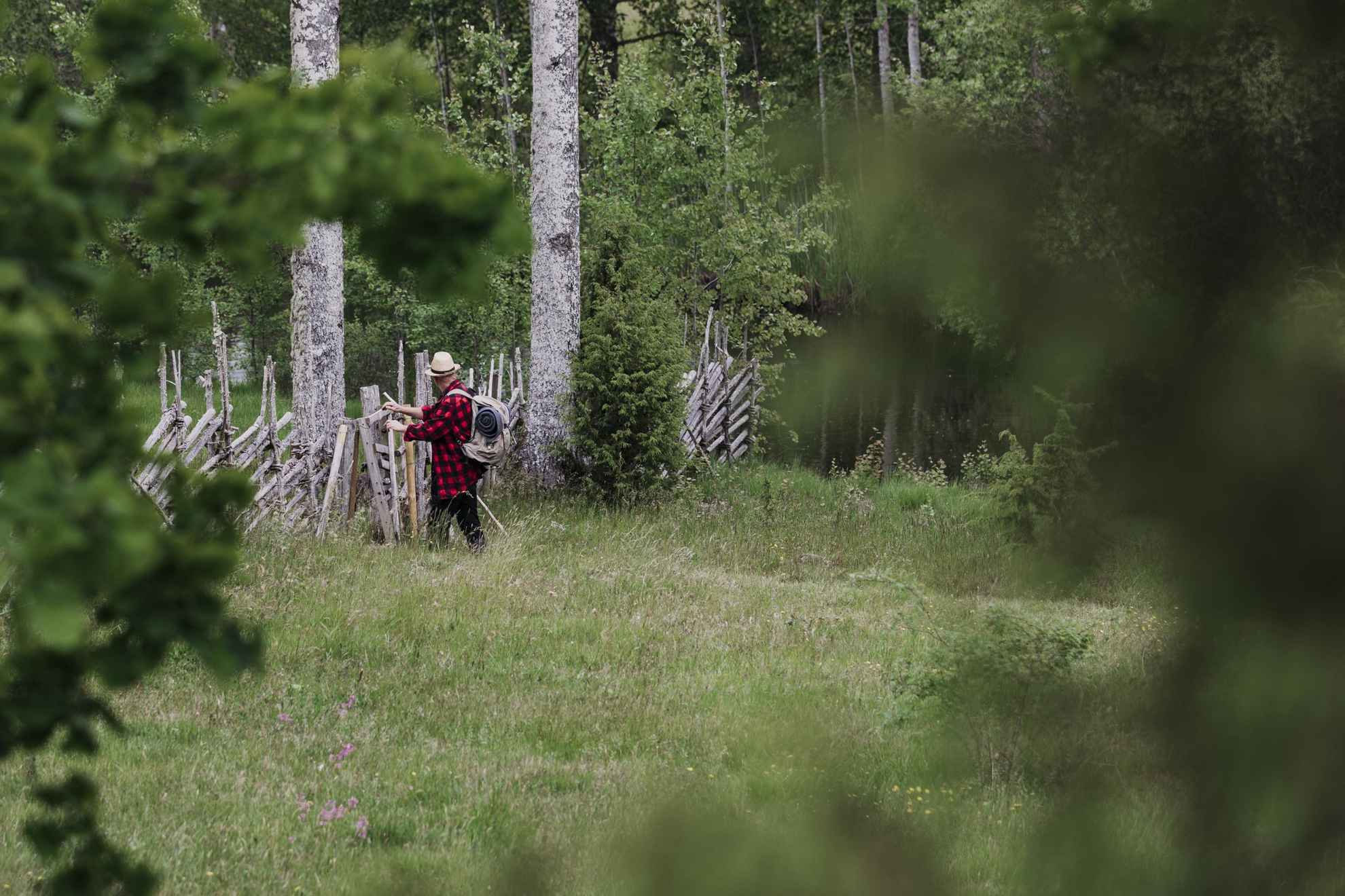 Een man met een rugzak opent een poort in een hek op een wandelpad in de natuur dicht bij een bos.