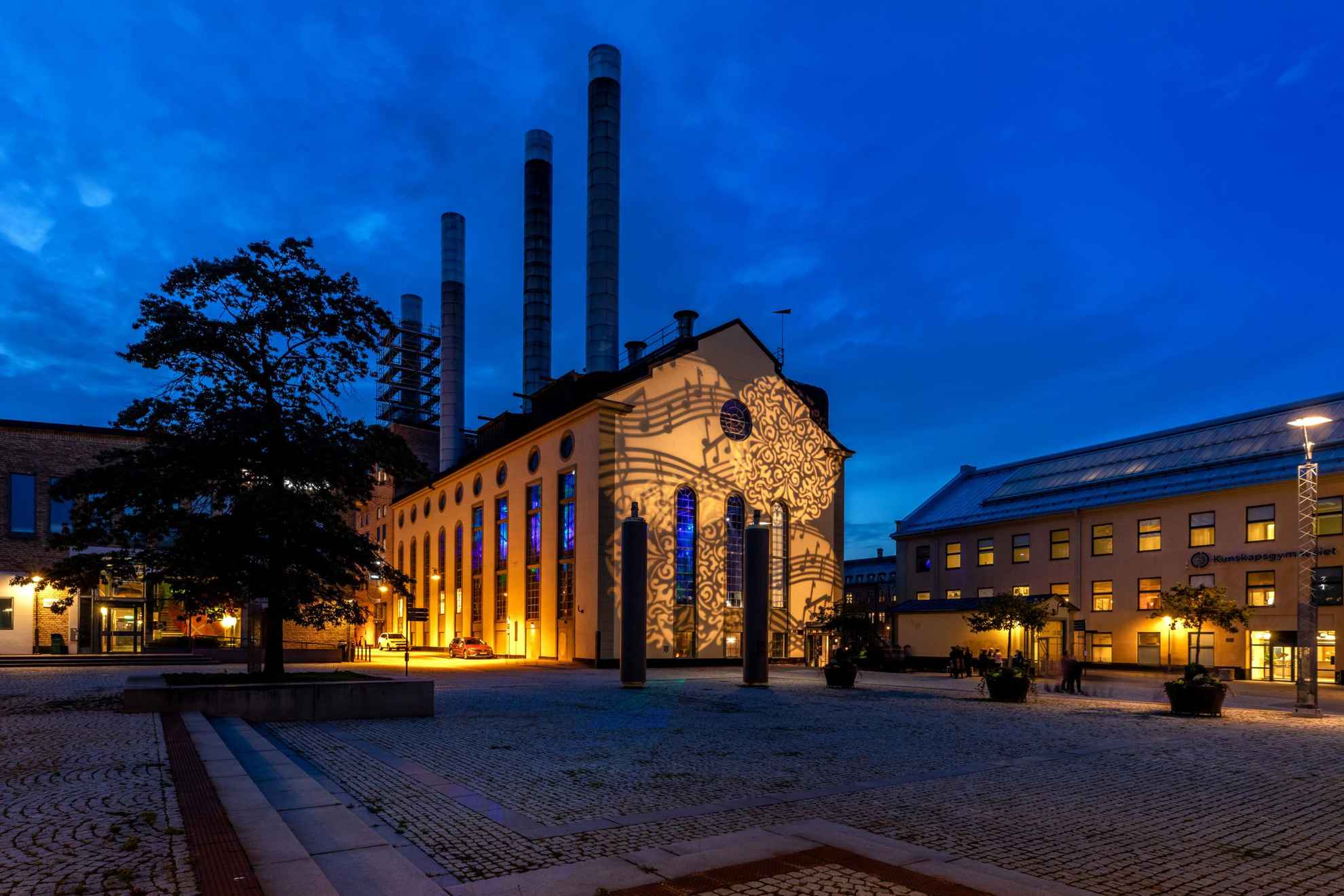 Een industrieel gebouw 's nachts verlicht door lichten die muzieknoten uitbeelden.
