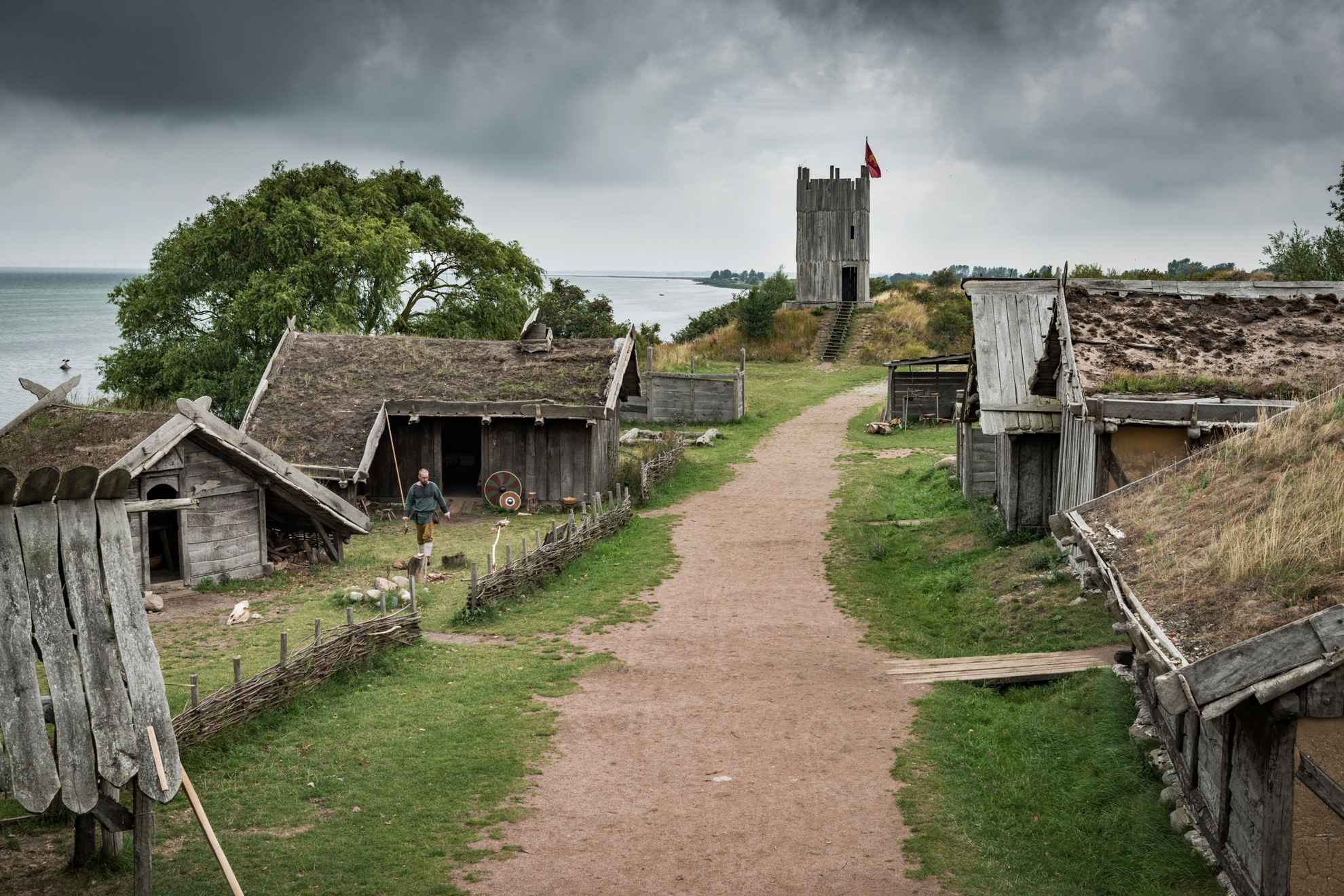 Een onverharde weg die door een traditioneel vikingdorp leidt met houten huizen met met gras bedekte daken.