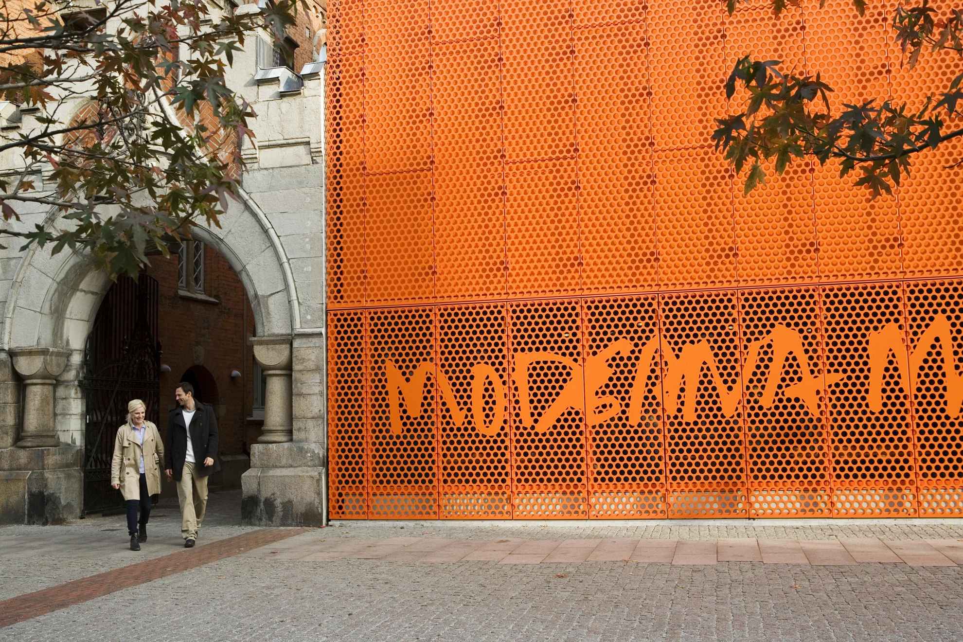 Een man en een vrouw lopen naar buiten en langs het oranje bord van het Moderna Museet in Malmö.