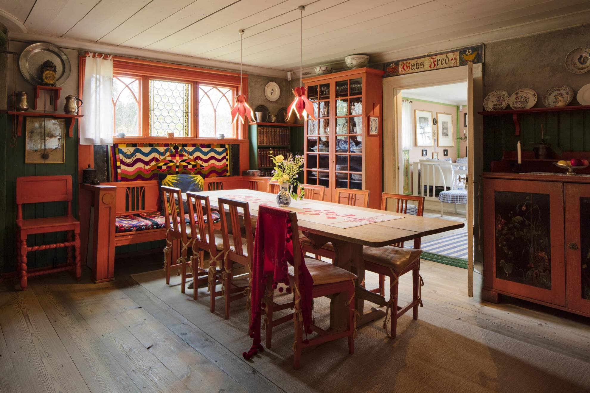 Historisch Zweeds interieurontwerp bij Lilla Hyttnäs, met een grote eettafel, rood houten meubilair en historisch porselein op sommige muren.