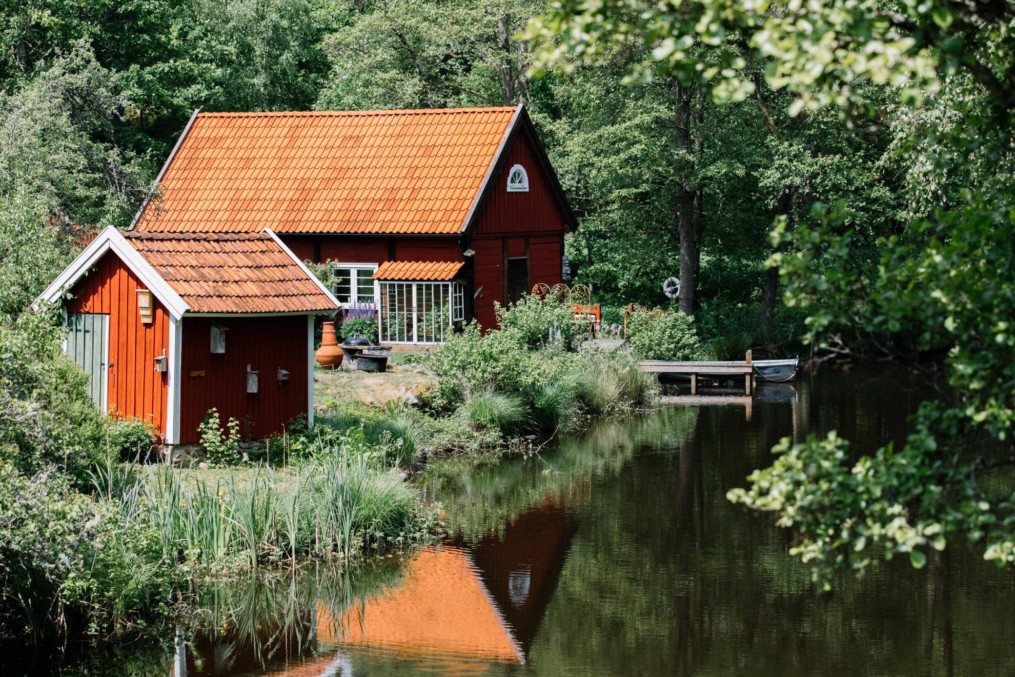 Naast een meer met een weelderig bos eromheen staan een traditioneel rood huisje en een klein rood gastenverblijf.