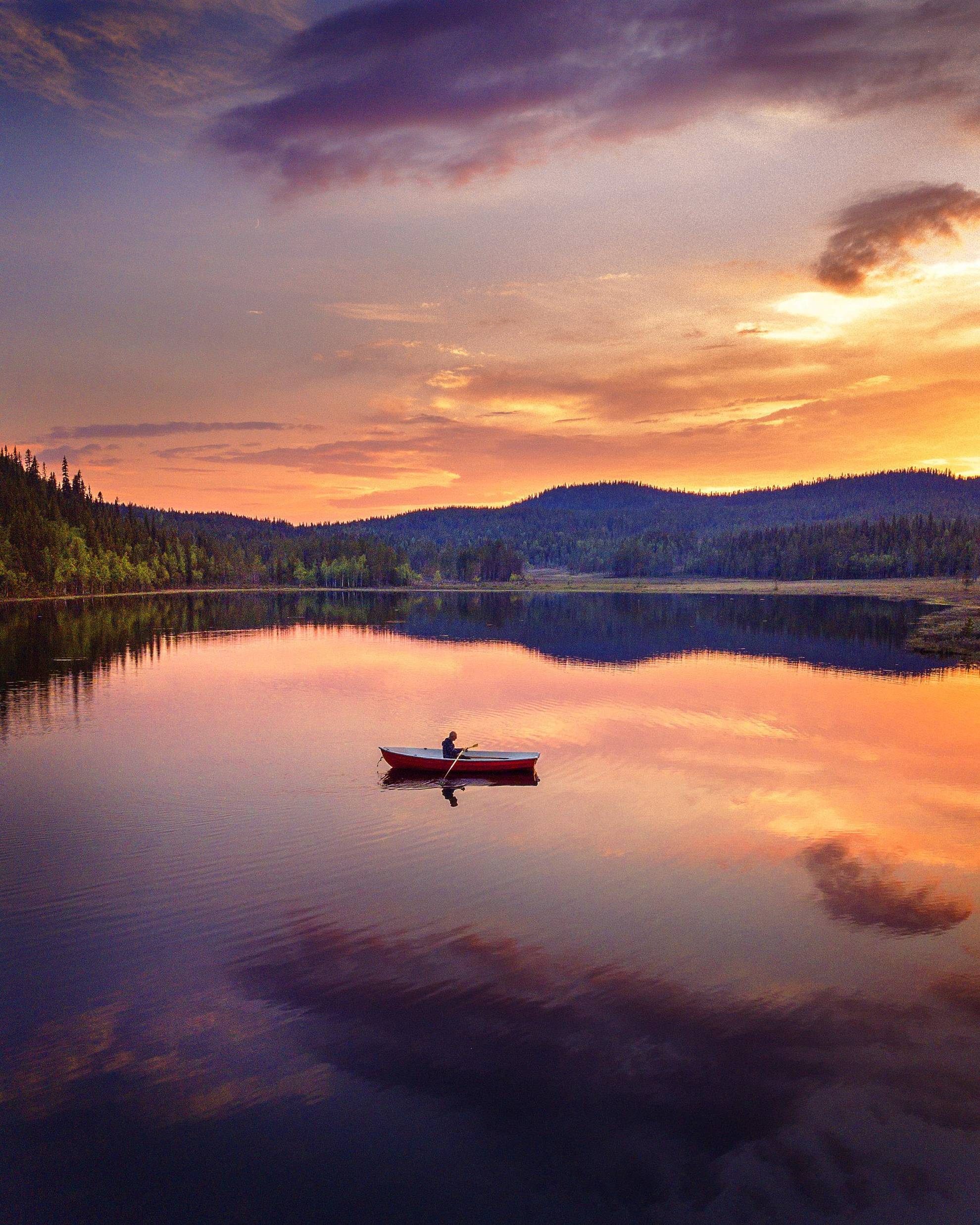 Een persoon roeit een boot op een gespiegeld meer onder de middernachtzon.