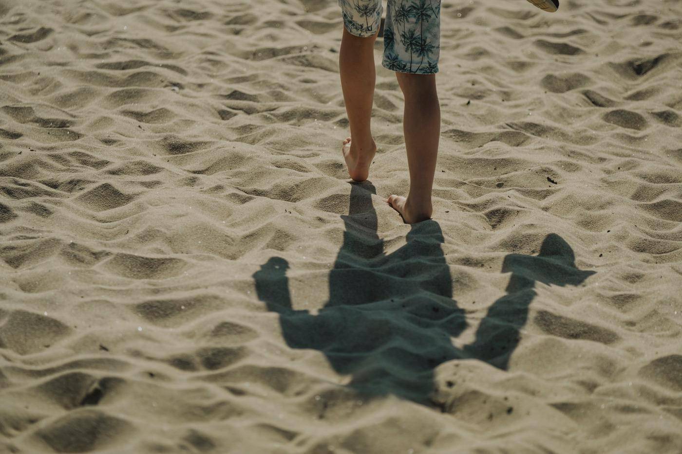 De benen en schaduw van iemand die op het zand loopt op het Borrby-strand in Skåne.