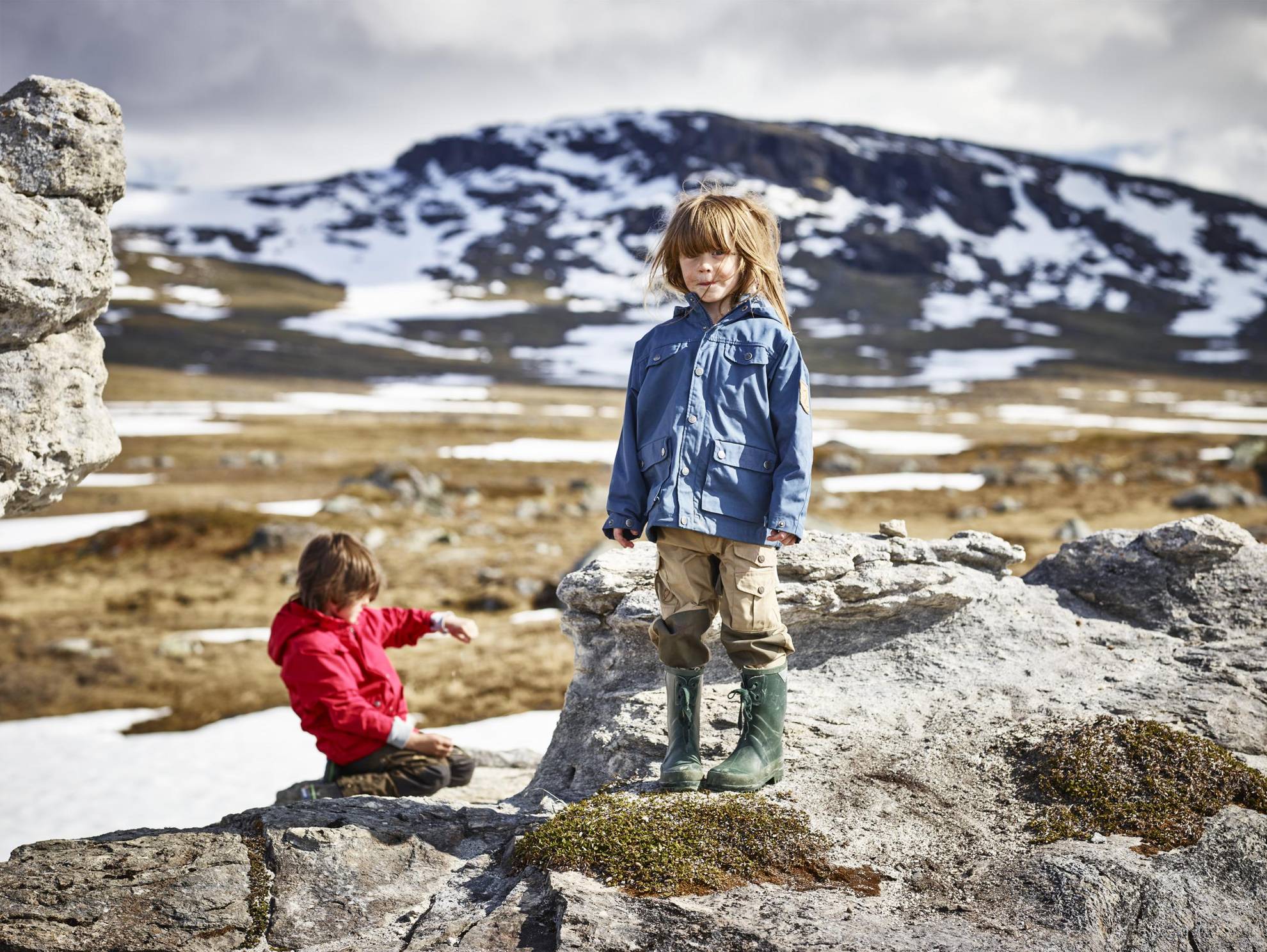 Two kids on a hike in Padjelanta in northern Sweden, surrounded by patches of snow and mountain peaks.