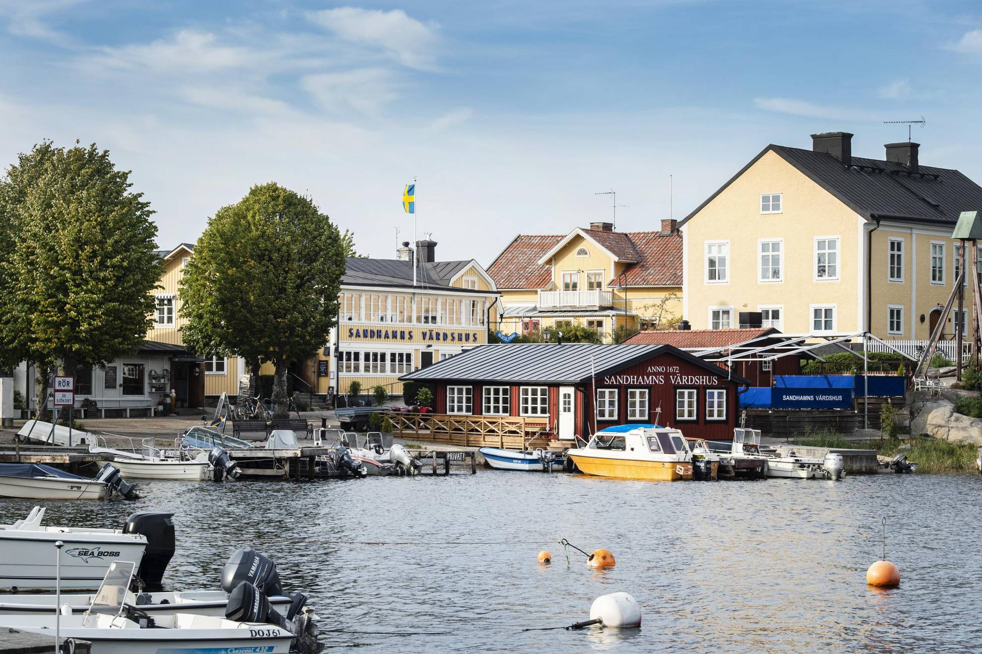 Huizen in geel en rood, gelegen bij een haven met veel kleine boten in Sandhamn.