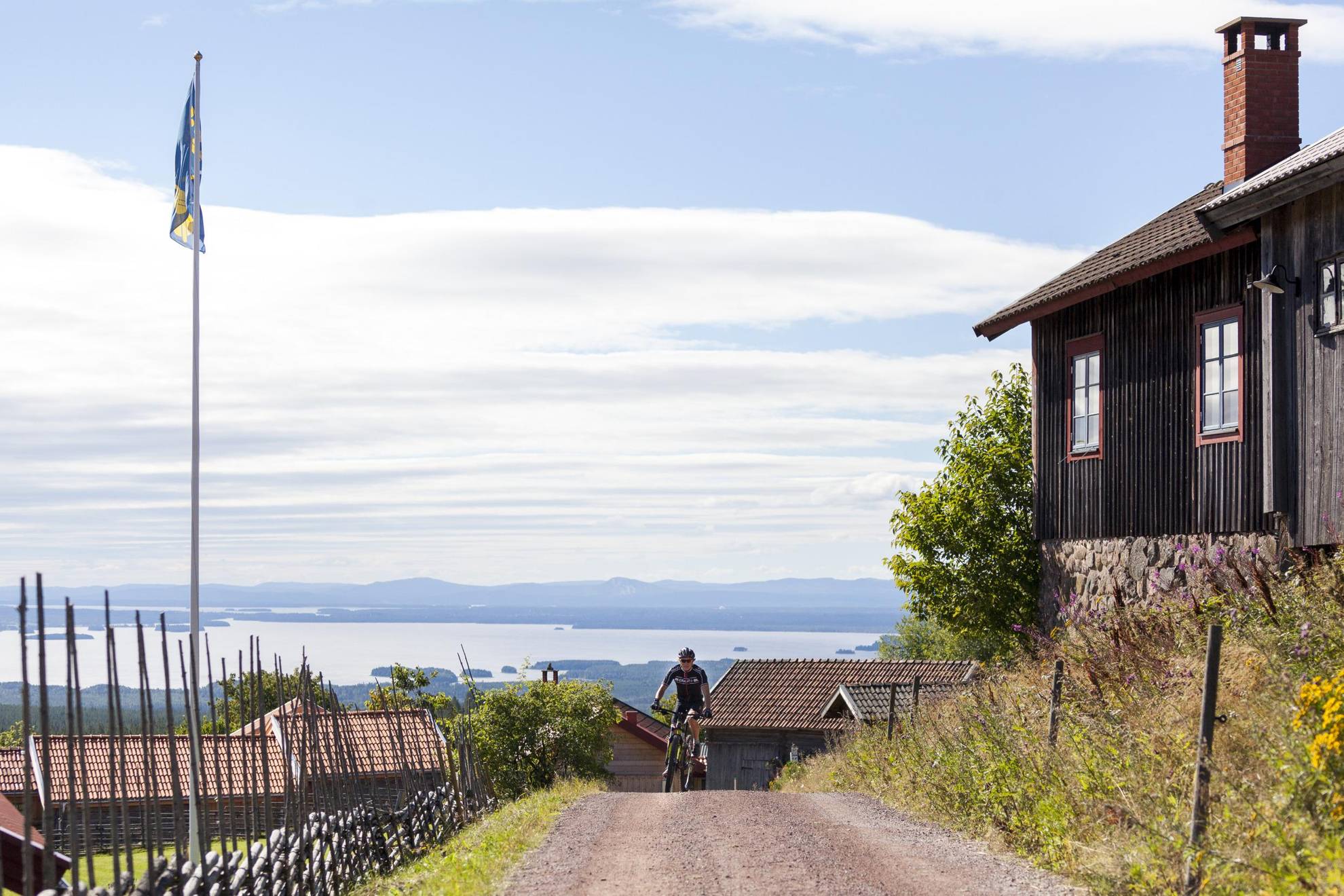 Een zicht op een meer en de bergen achter een persoon die op een weg een heuvel op fietst.