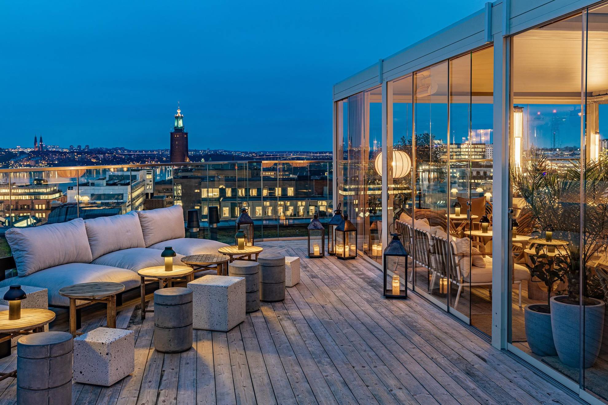 Een stijlvolle buitenbar op een dak met uitzicht over Stockholm en het stadhuis. Rechts zie je een gedeelte dat achter glazen wand zit.