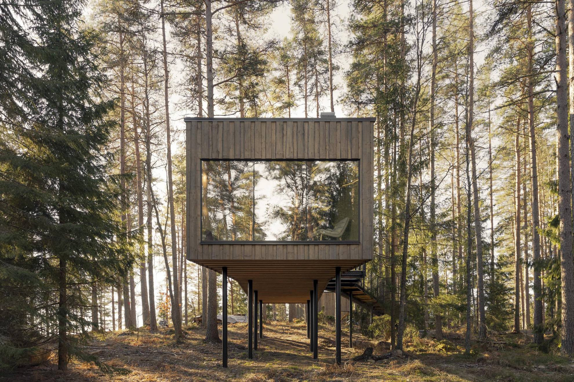 Een rechthoekige houten suite met een groot raam bevindt zich in een bos.