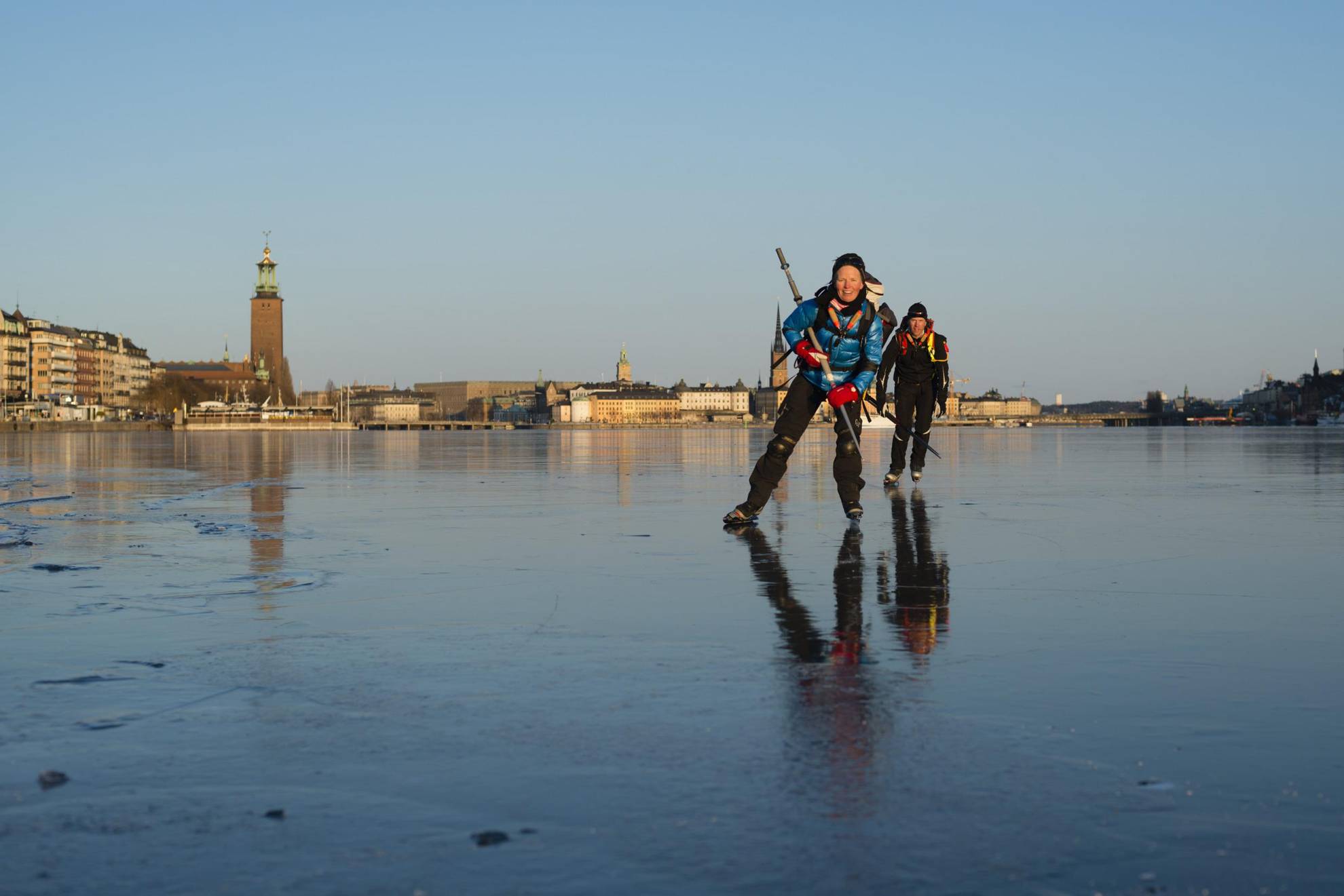 Twee schaatsers op het meer met op de achtergrond het stadhuis van Stockholm.