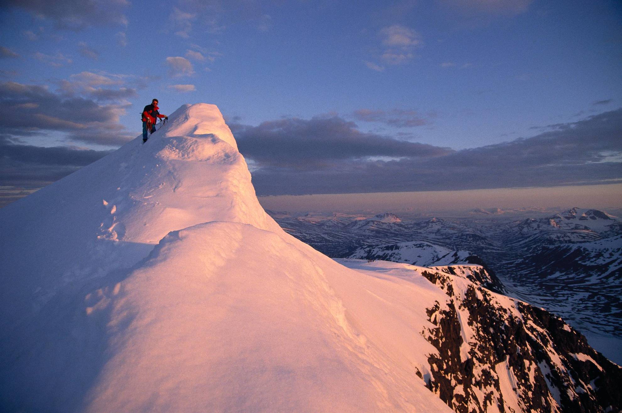 Een persoon staat op de top van een besneeuwde berg.
