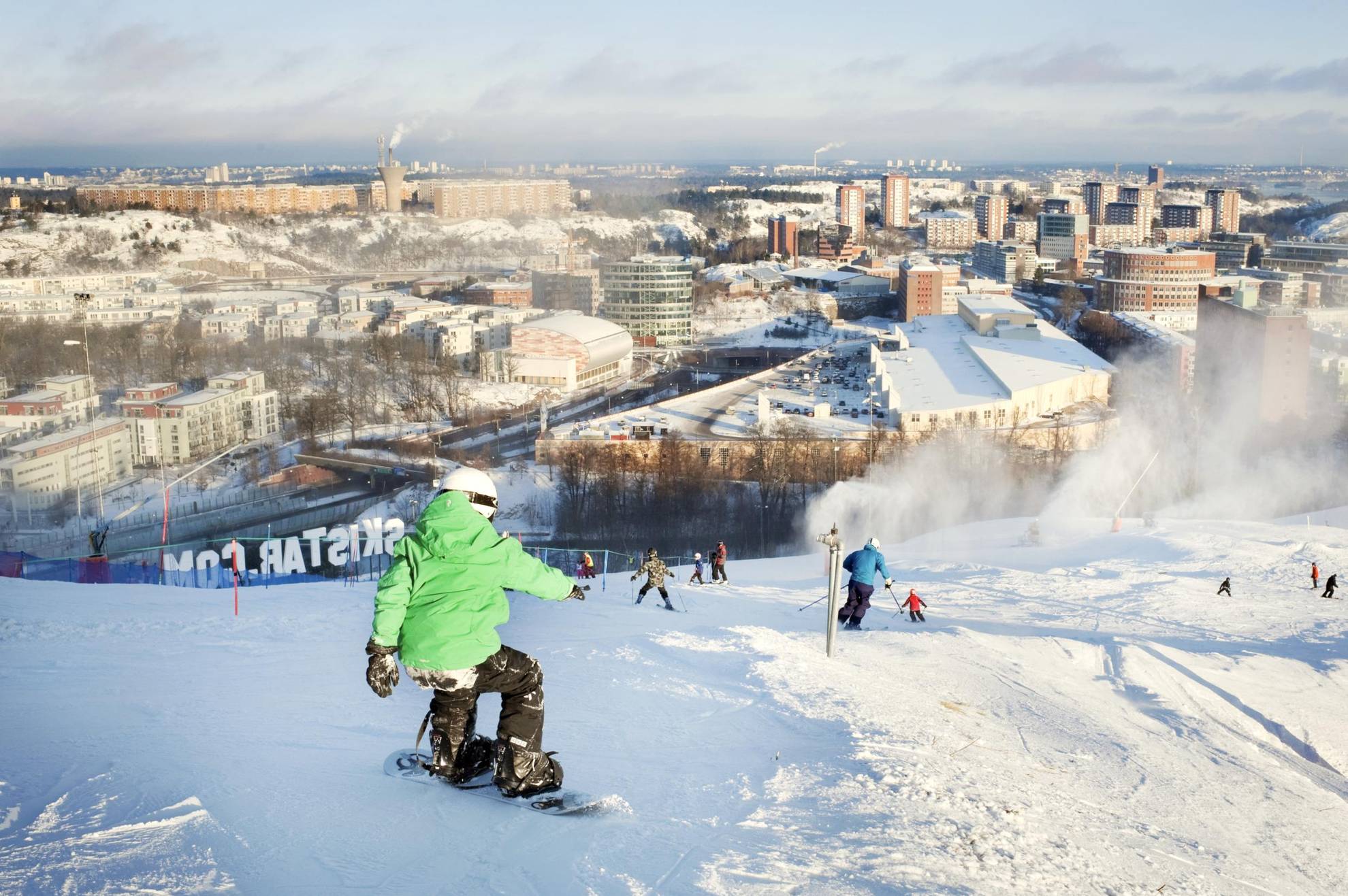 Mensen gaan op ski's en snowboards de hellingen van Hammarbybacken af en kijken uit over het centrum van Stockholm.