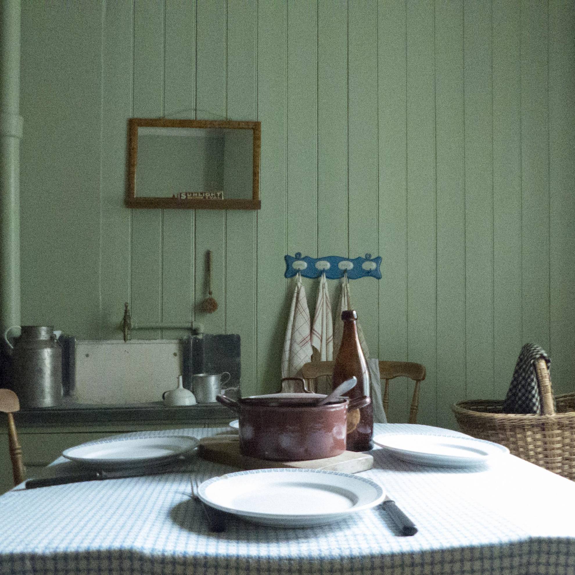 In een arbeiderswoning in de eerste buitenwijk van Göteborg in de 19e en 20e eeuw. Een gedekte tafel met een ijzeren pot in het midden. Aan een groene houten wand hangt een spiegel.