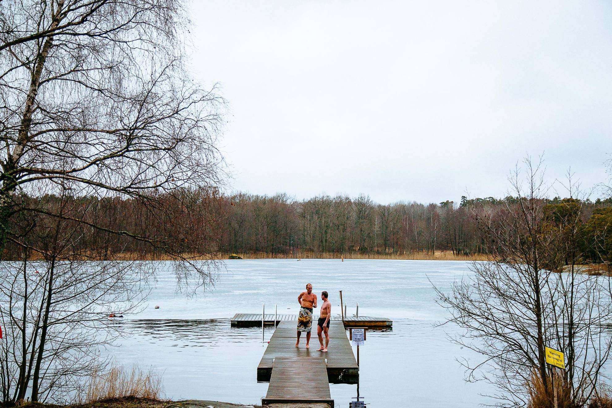 Twee mannen lopen op een steiger nadat ze in de winter in een bevroren meer hebben gezwommen.