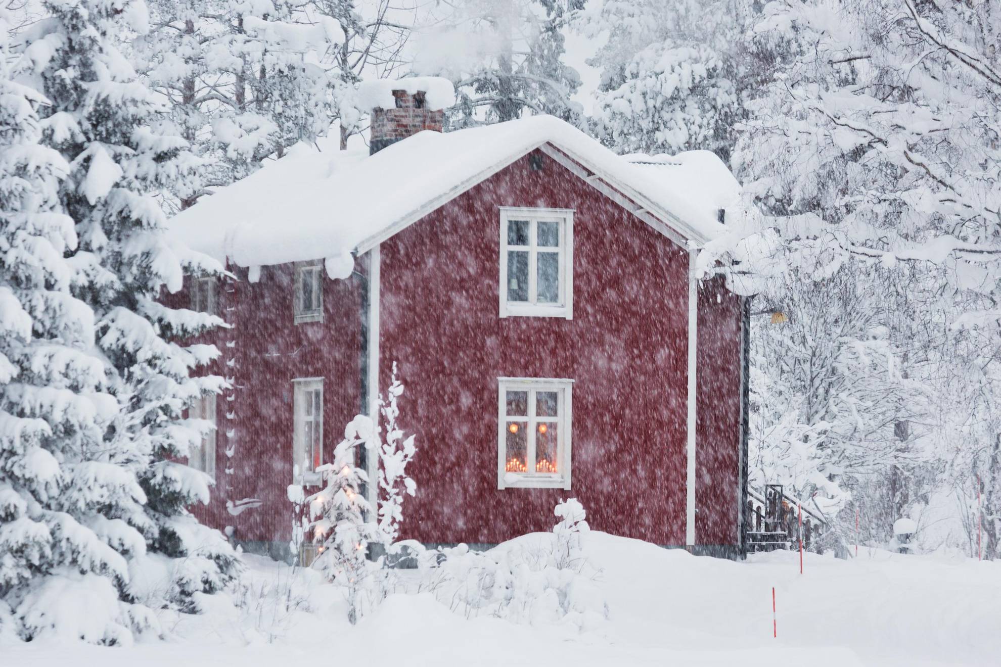 Een rood huis met witte biezen bedekt met sneeuw tijdens sneeuwval.