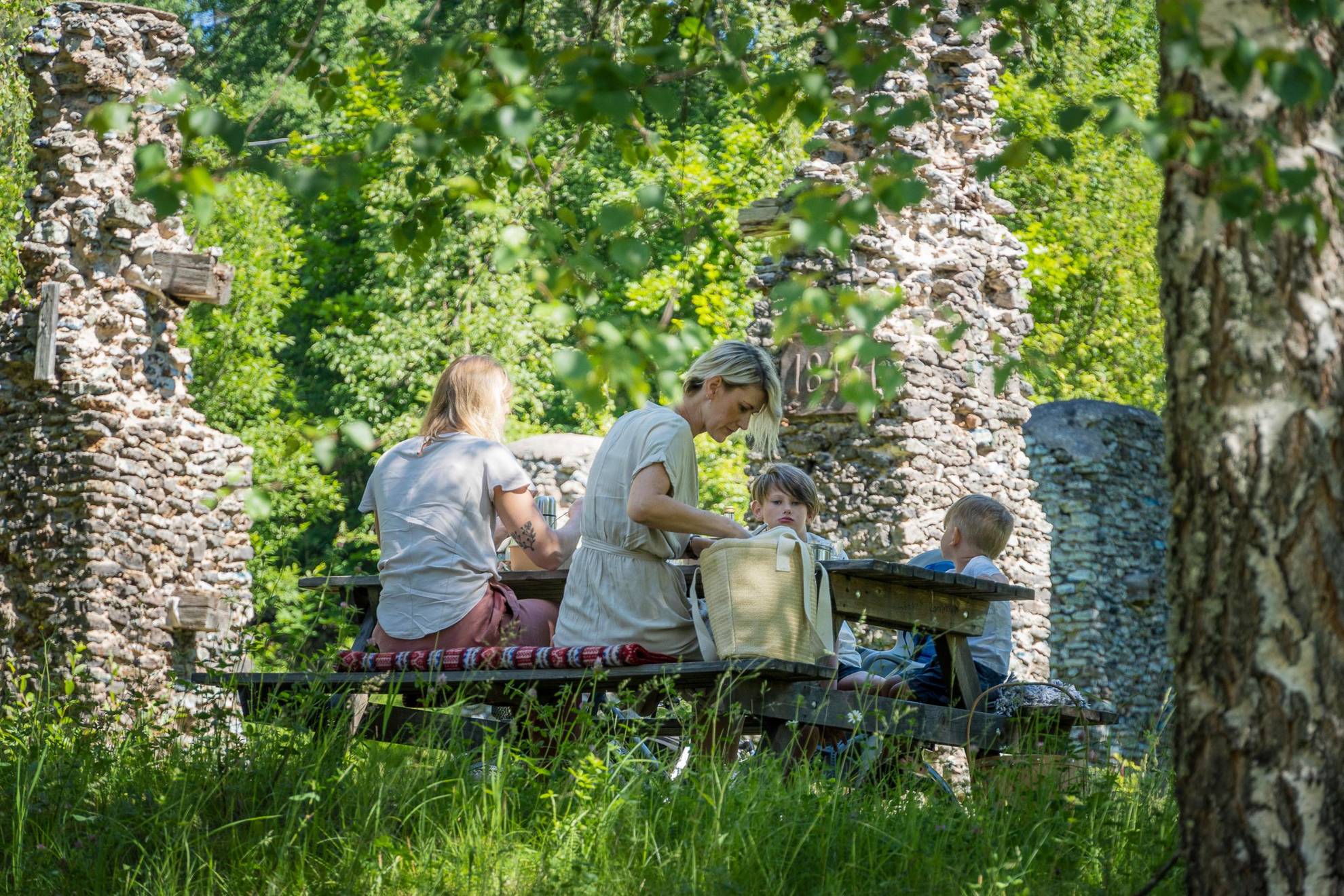 Een gezin aan een picknicktafel in het bos, omgeven door weelderig groen.