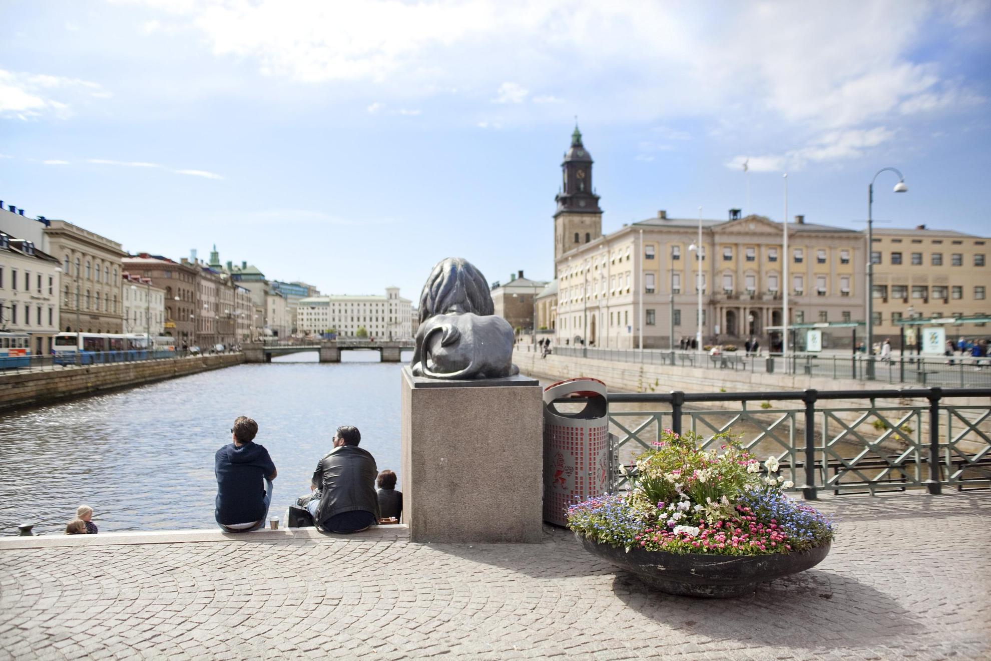Twee mensen zitten op Lejontrappan in Brunnsparken. Op de achtergrond is het stadhuis van Göteborg zichtbaar.